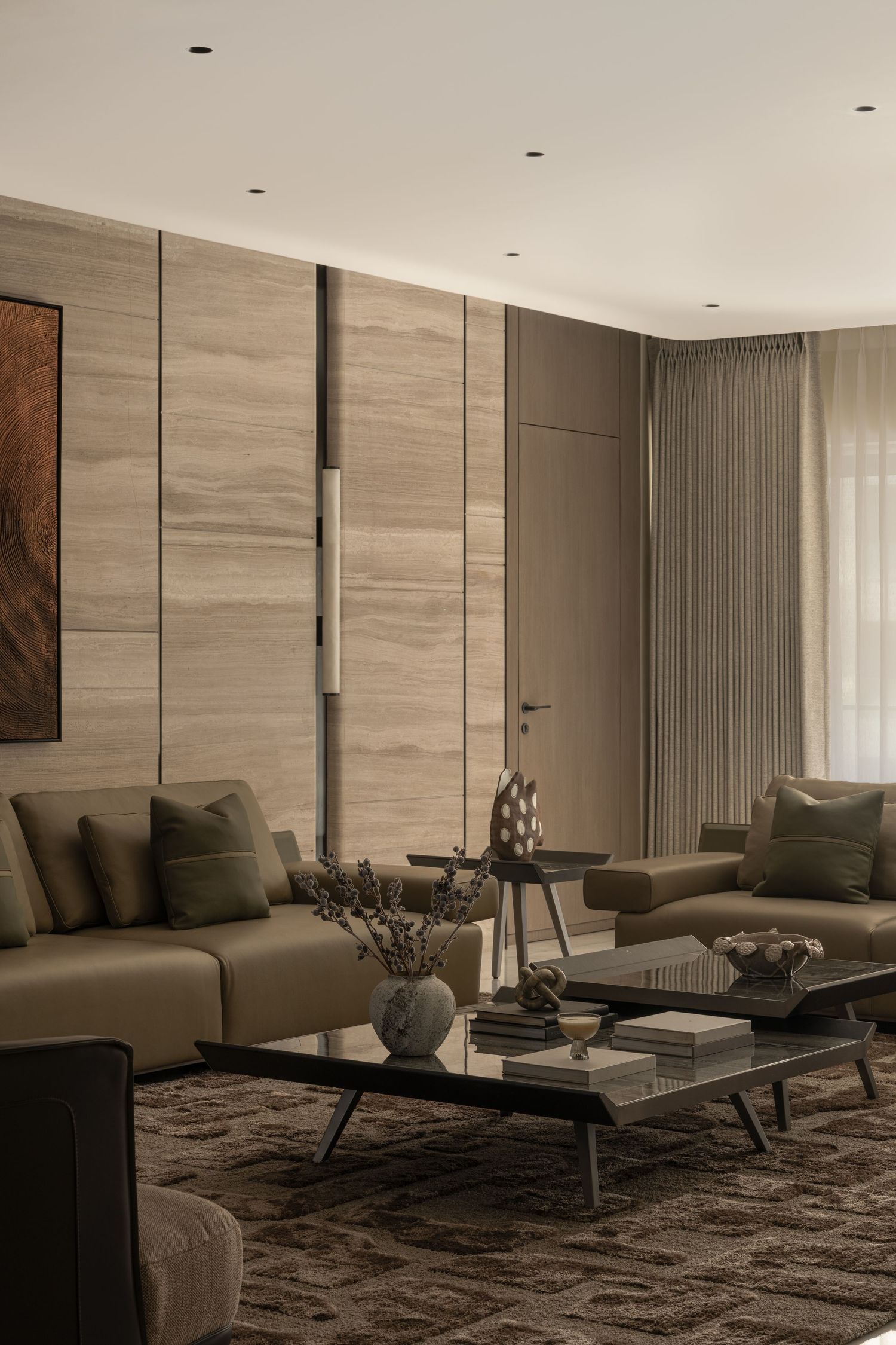 Sophisticated living room with travertine panel walls, olive green sofas, and glass coffee table.