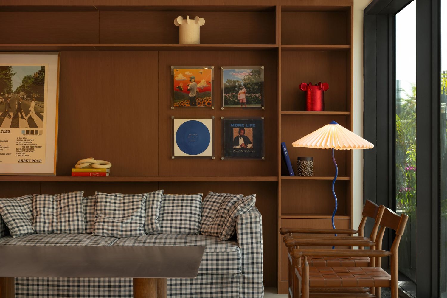 Retro lounge with plaid sofa, wooden bookshelf displaying vinyl records, and a warm floor lamp.