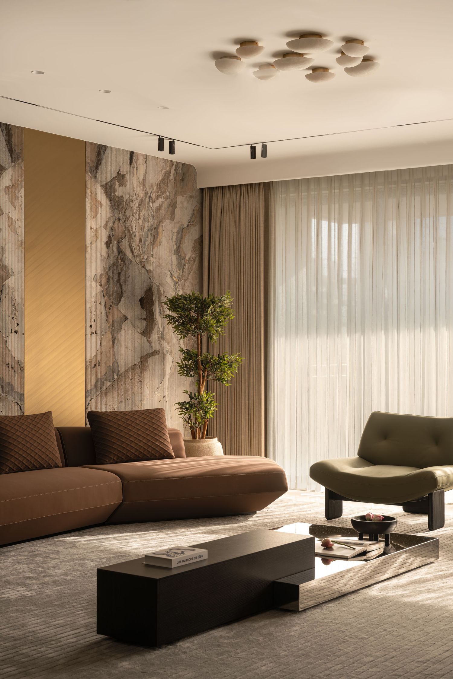 Luxurious living room with brown curved sofa, marble accent wall, gold panel, and organic ceiling fixture.