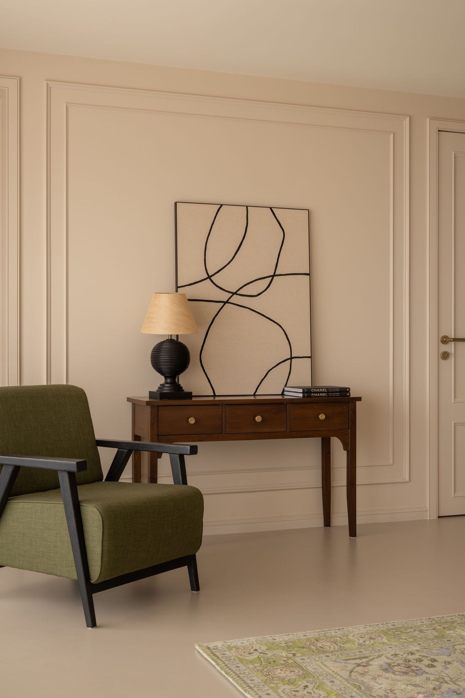 Classic living room with green armchair, walnut console table, black table lamp, and abstract line art painting.