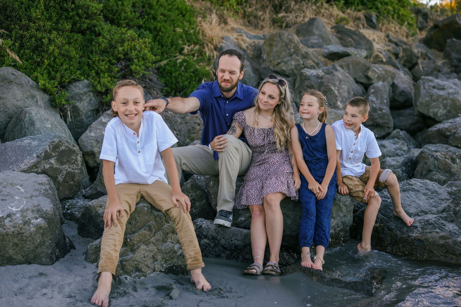Casual family portrait session on rocky beach with water in background.