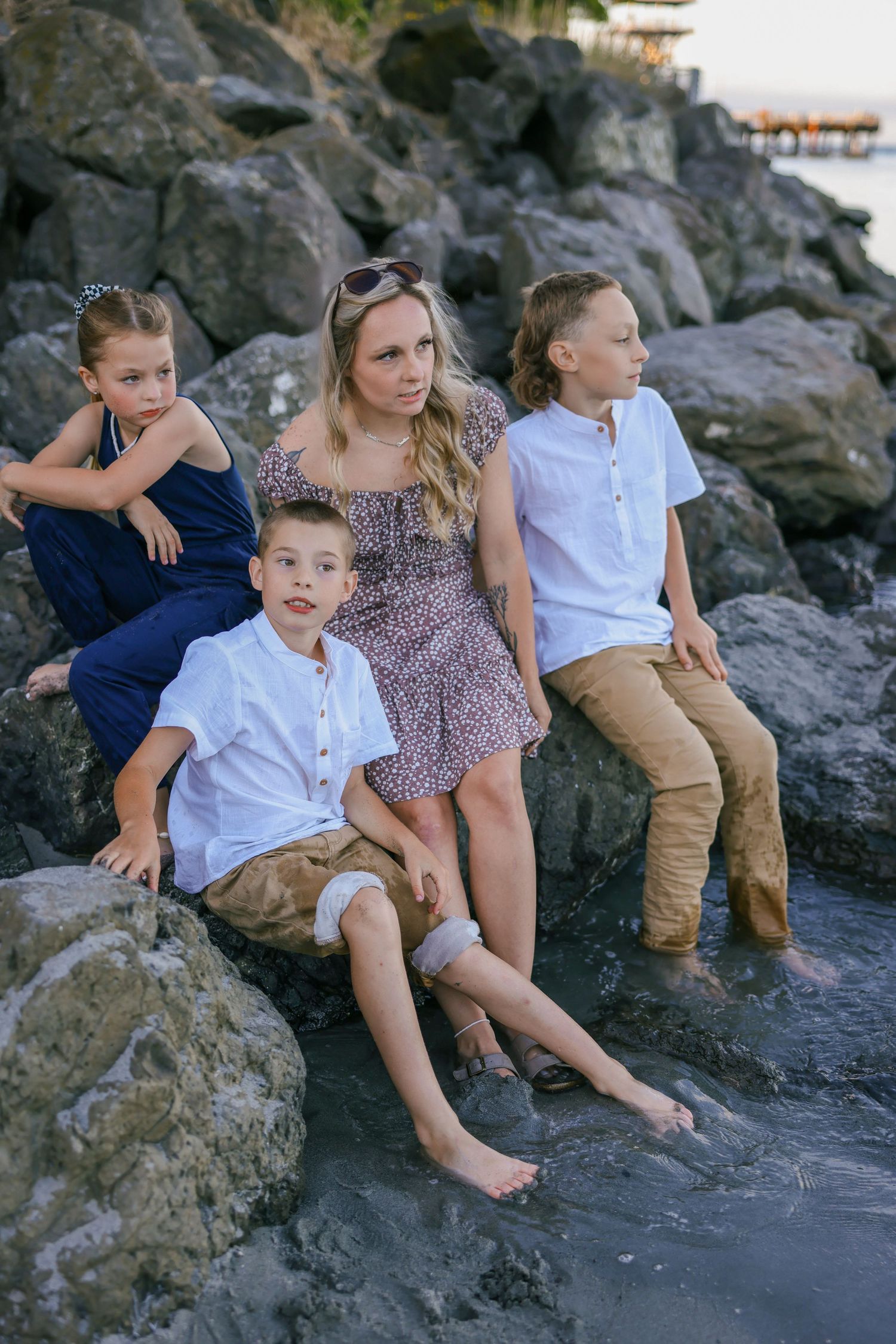Playful family photos on rocky beach with children sitting near water.