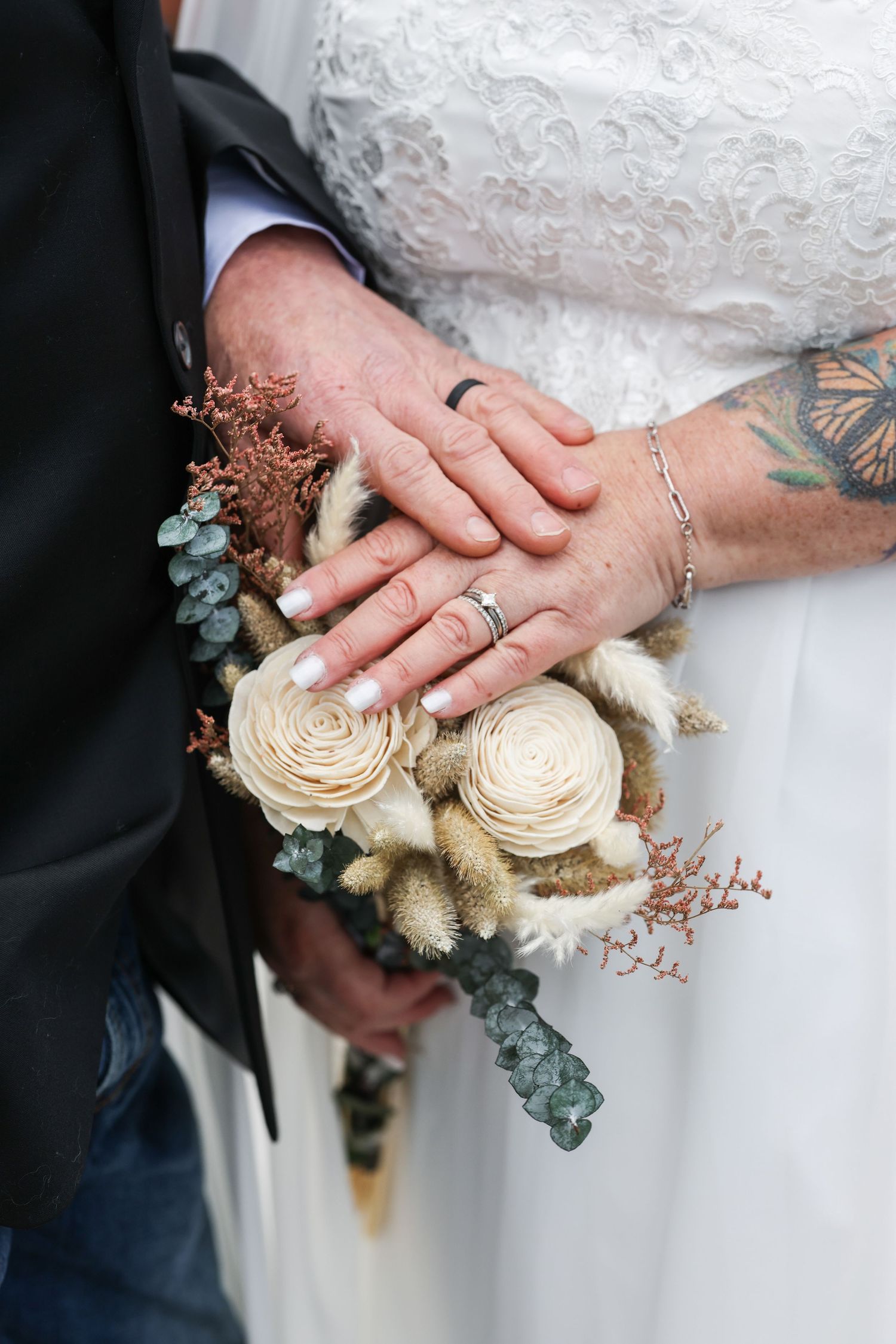 Close-up of hands holding a delicate cream-colored bouquet with dried flowers and eucalyptus.