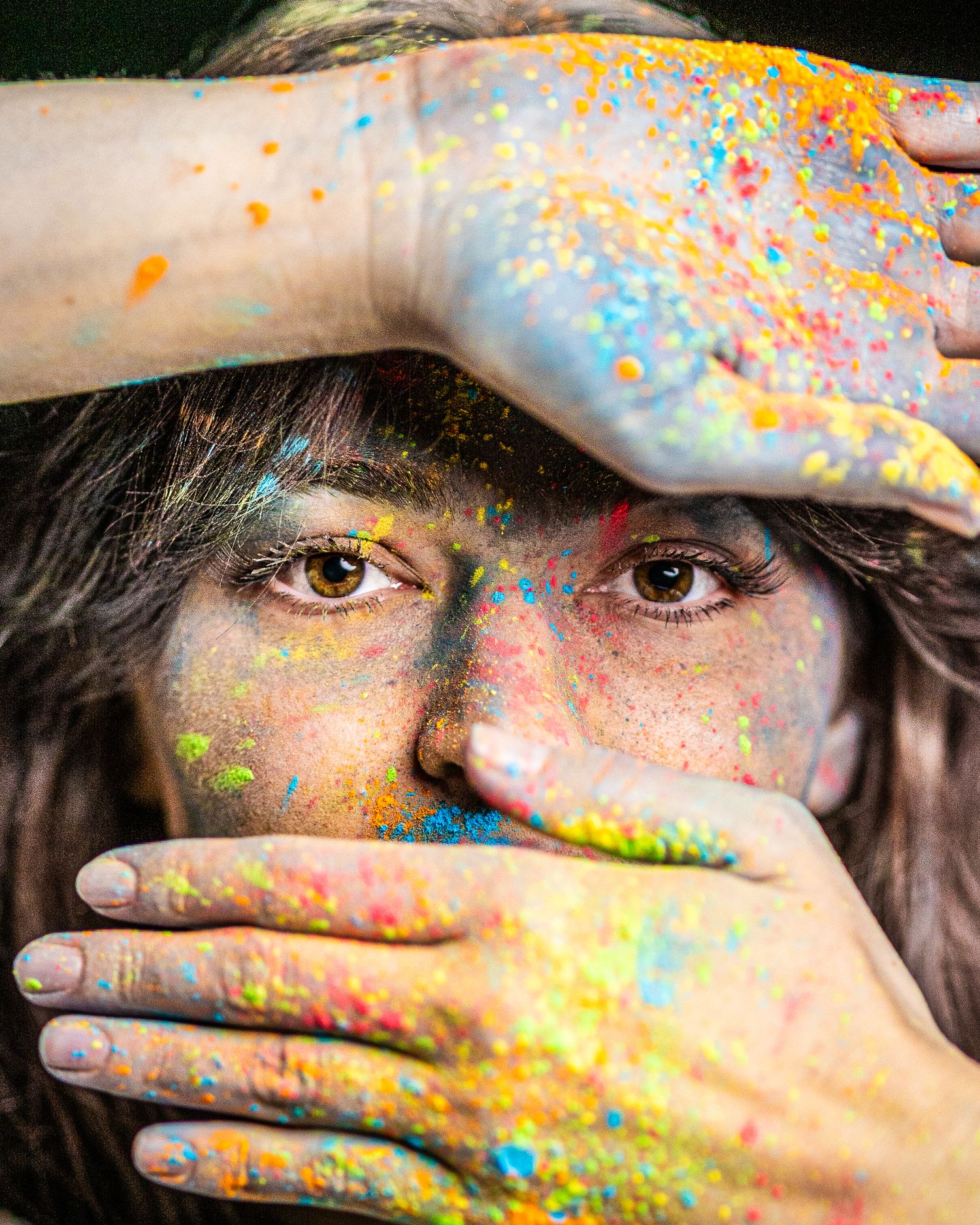 Close-up portrait with colorful powder paint covering hands and face.
