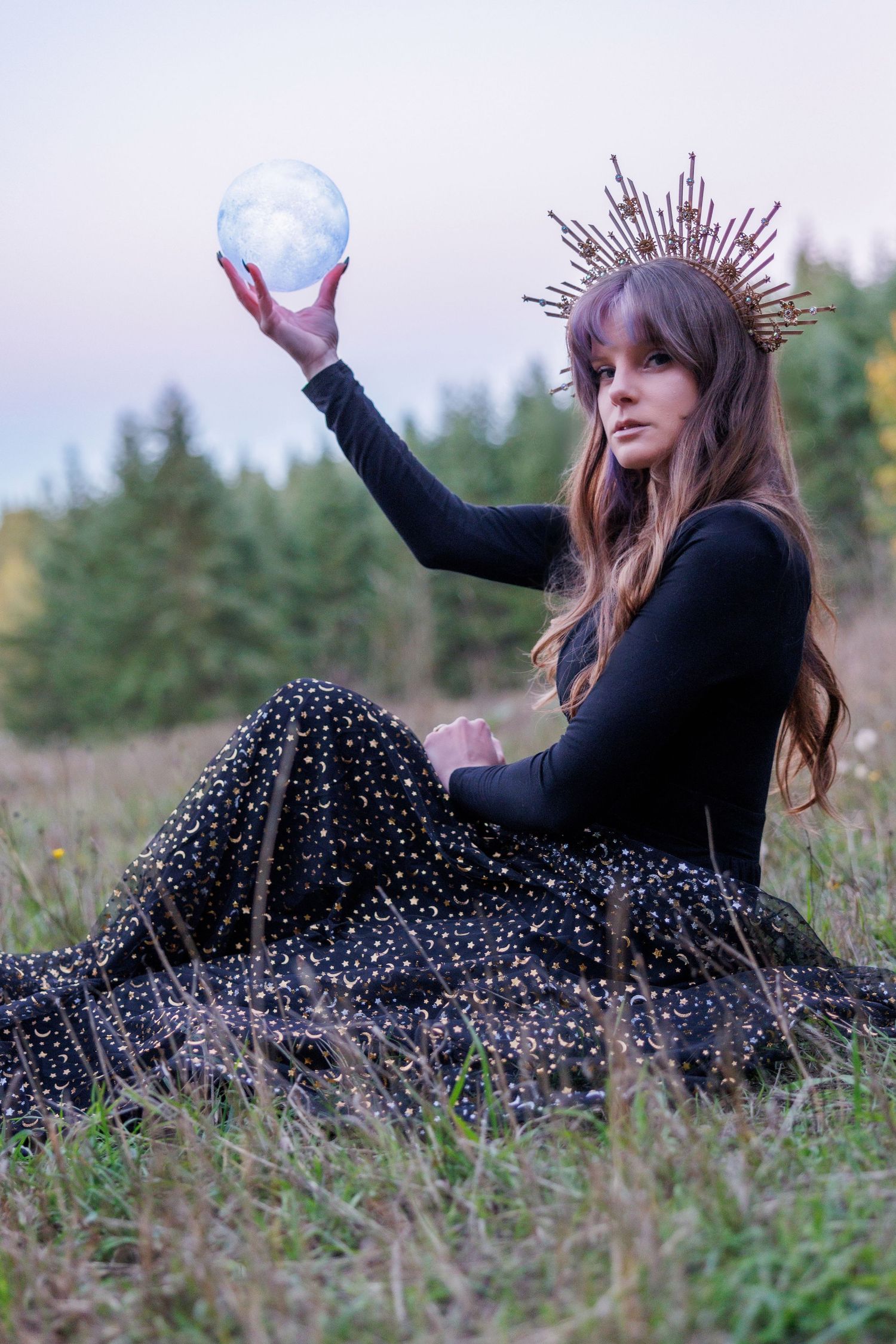 A person in a polka dot dress lies in a grassy field with a crown-like accessory, making expressive poses outdoors.