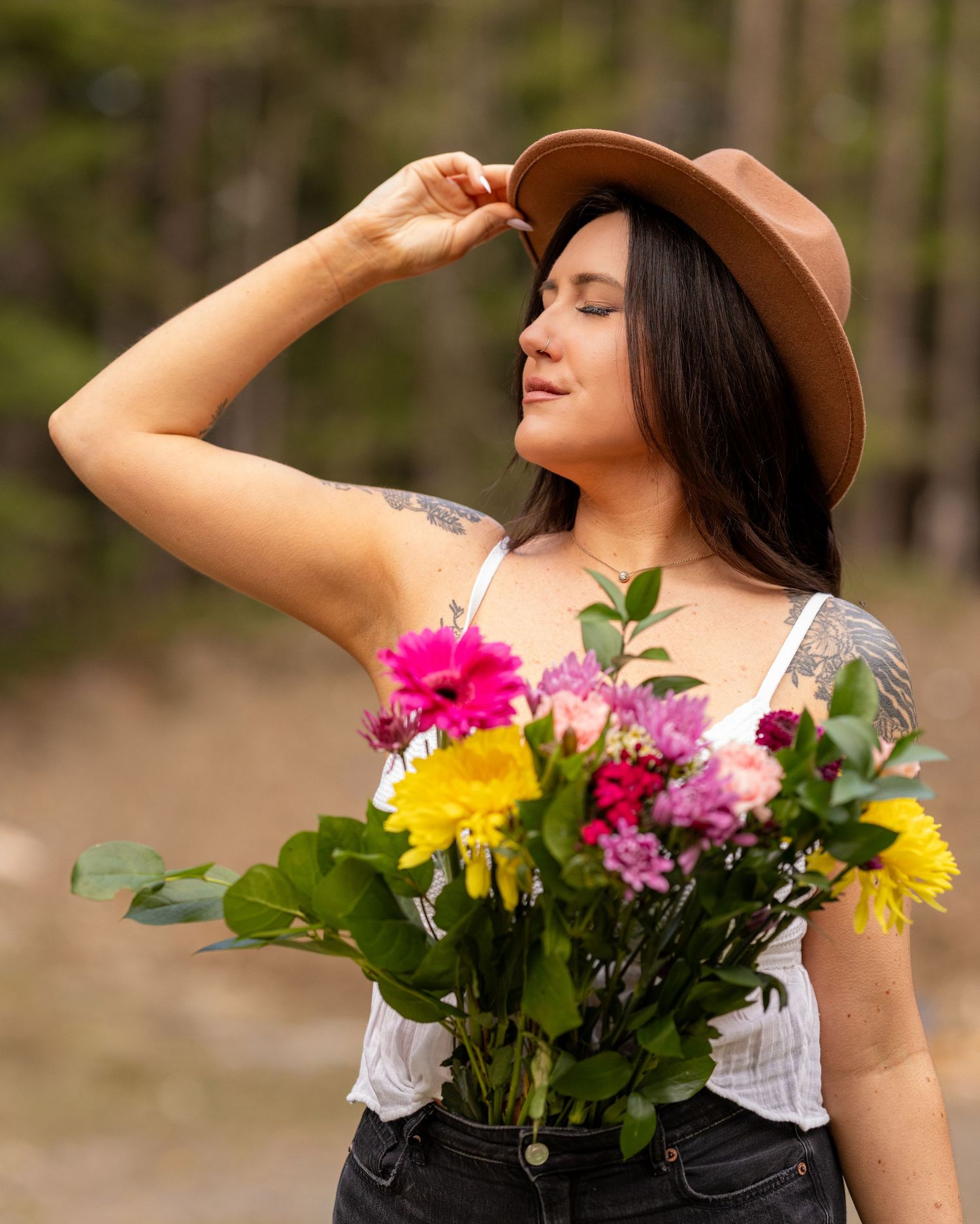 Woman in brown hat holding colorful flowers in outdoor nature setting.