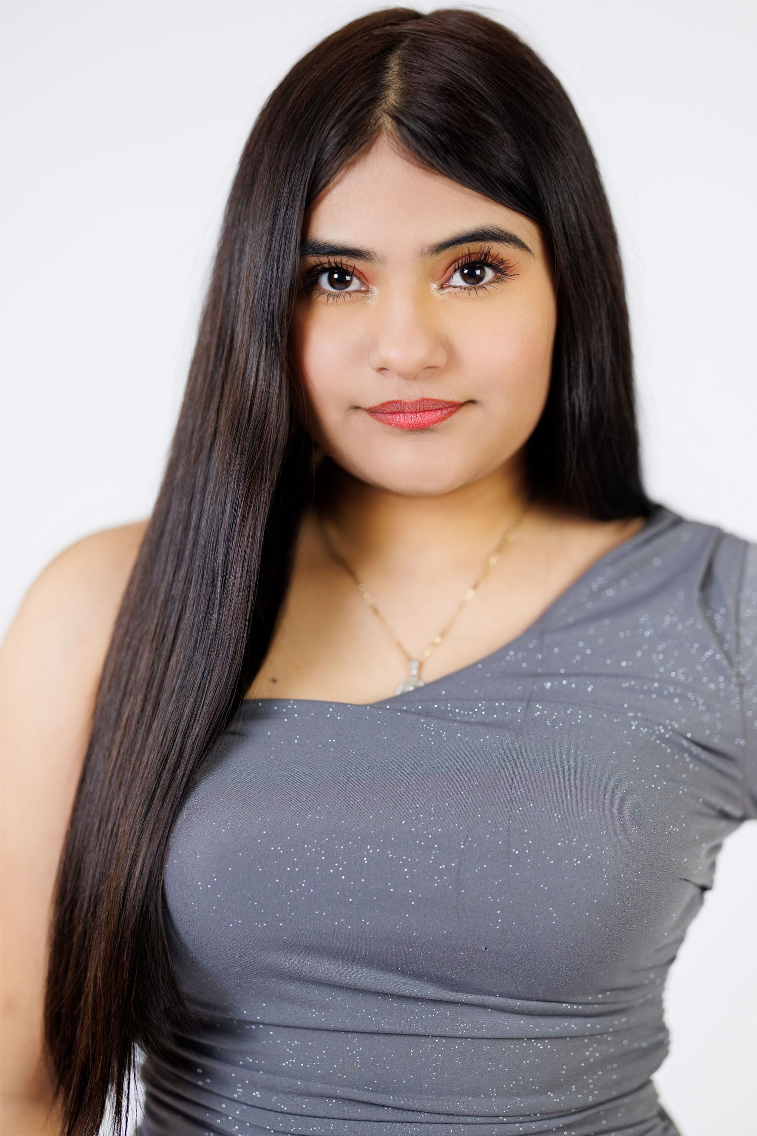 Portrait of a young woman with long straight black hair wearing a gray top against a white background.