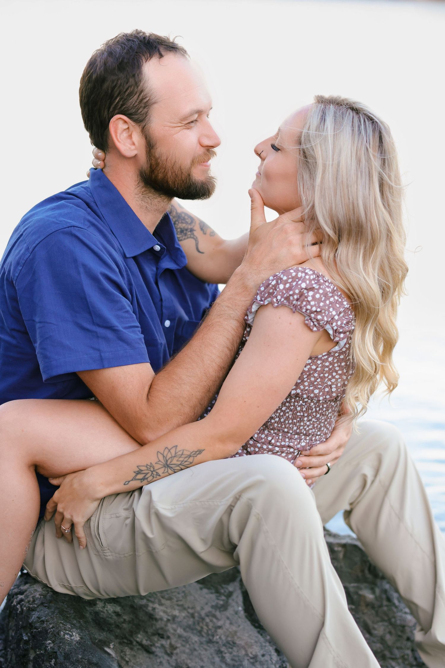 A romantic couple sharing an intimate moment while sitting on coastal rocks.