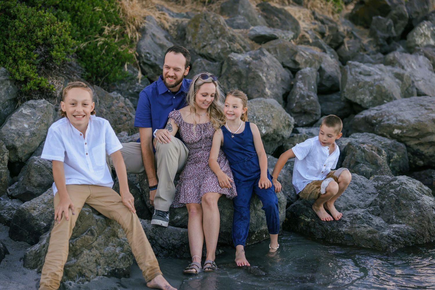 Family sitting together on large coastal rocks during golden hour photo session.