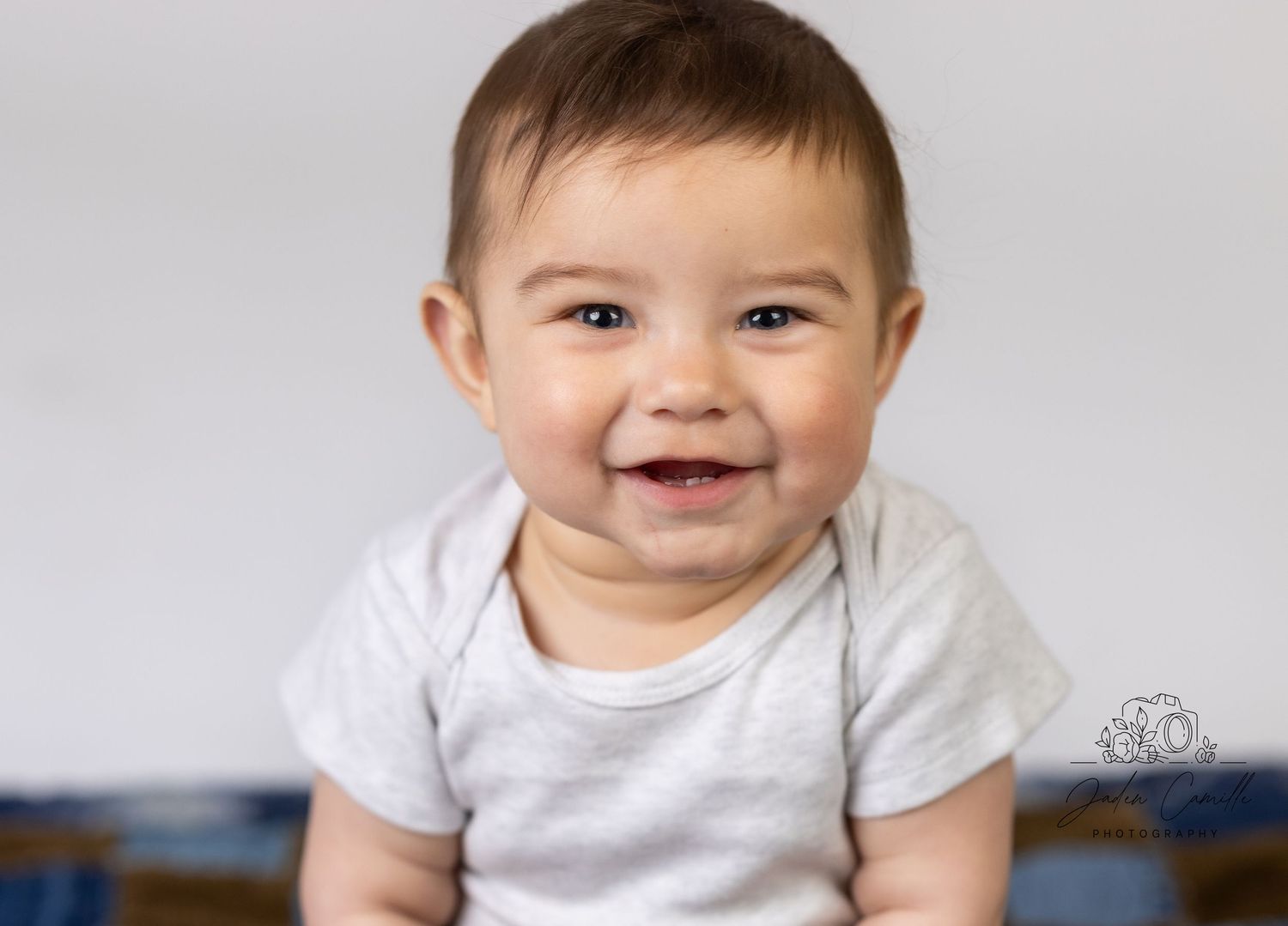 Baby in white onesie smiling at camera against light background.