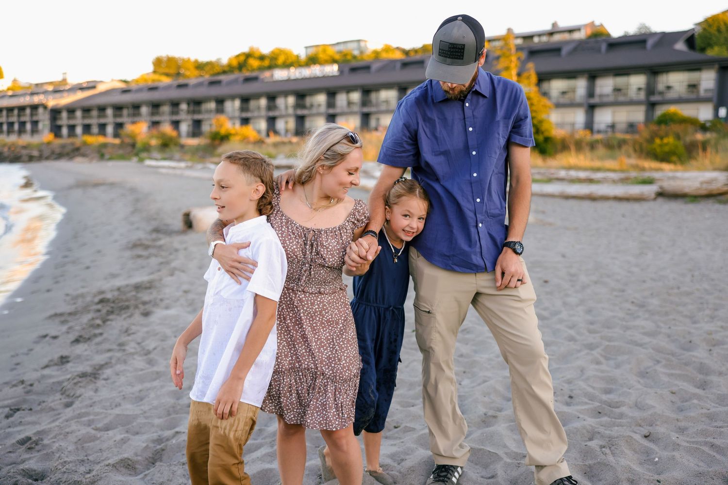 A family enjoying a playful moment together on a beach with buildings visible in the background.