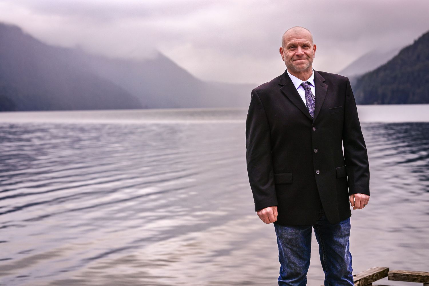 Overcast mountain lake landscape with couple on wooden dock during wedding ceremony.