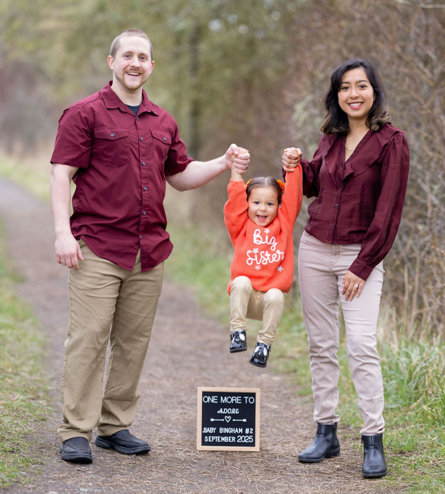 Family walking and playing together on outdoor path during pregnancy announcement photoshoot.