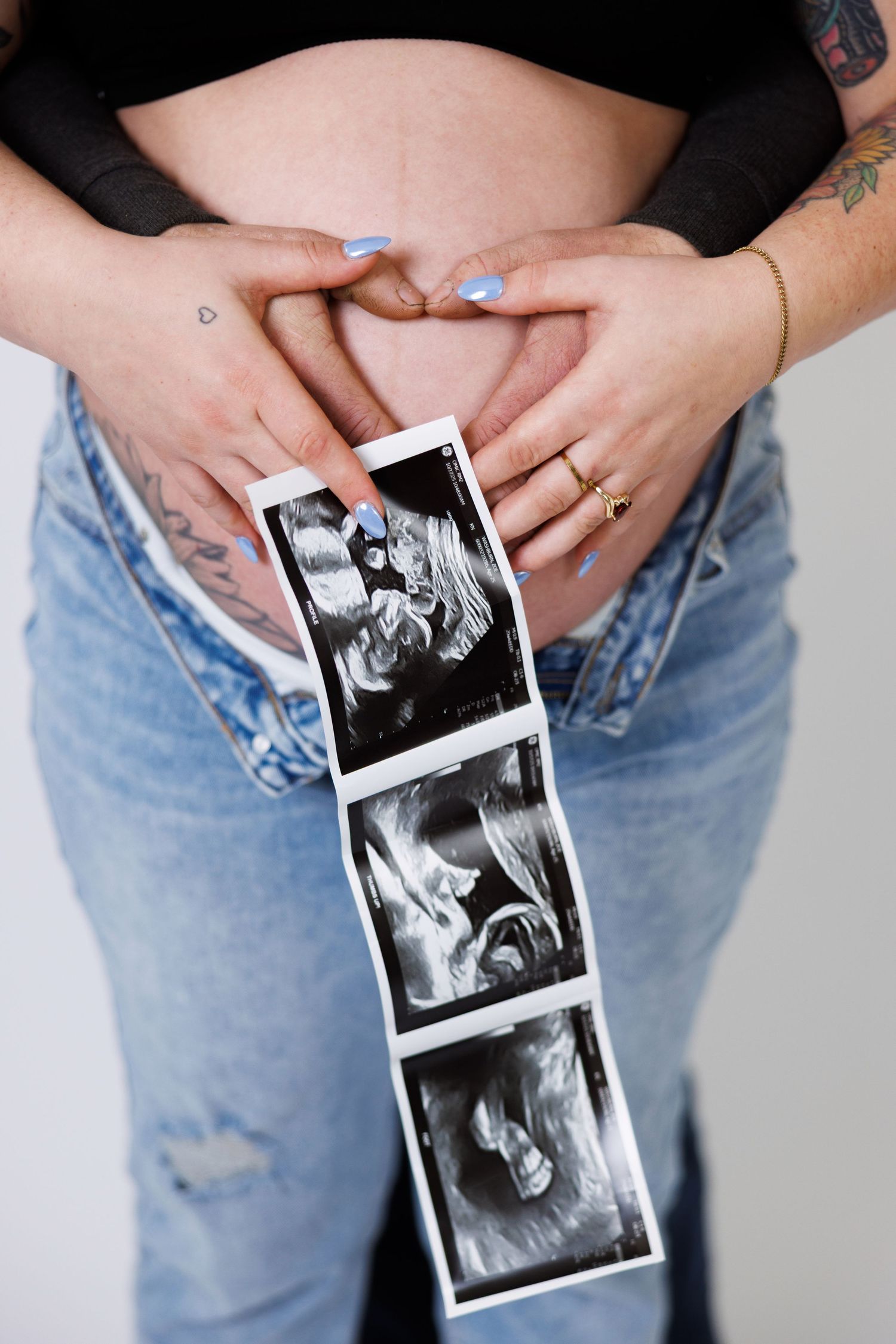 Hands holding ultrasound photos over a pregnant belly while wearing ripped jeans and a black top.
