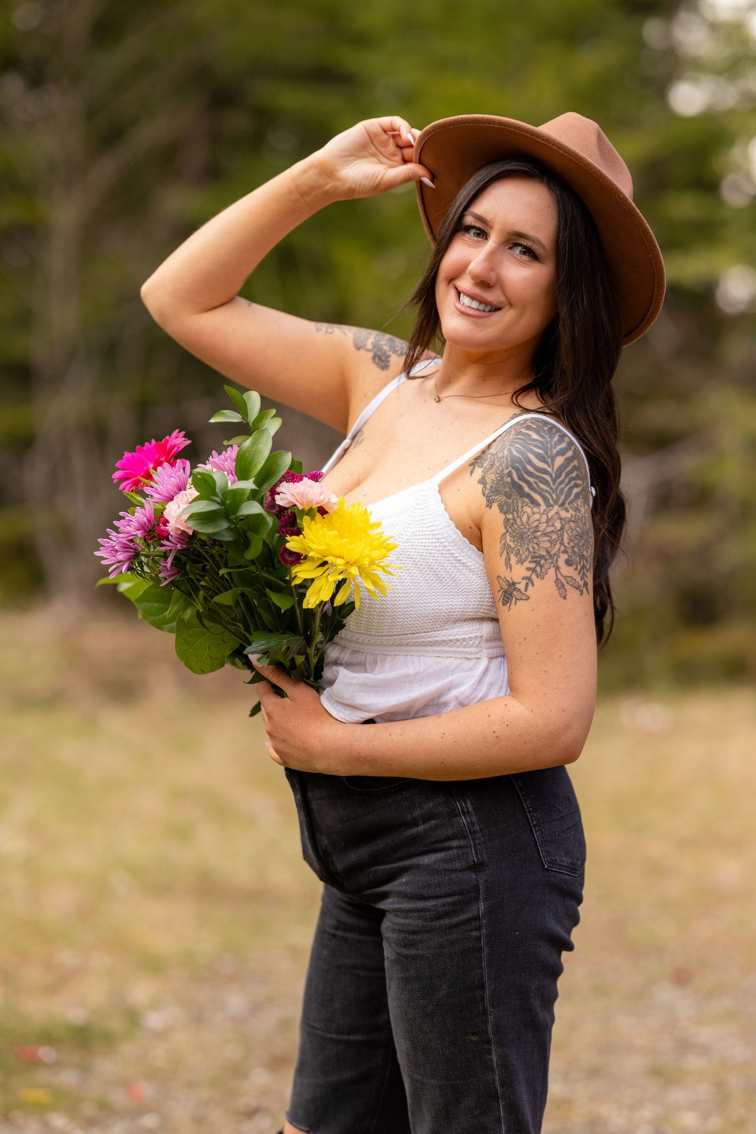 Woman wearing brown hat poses with vibrant bouquet against natural backdrop.