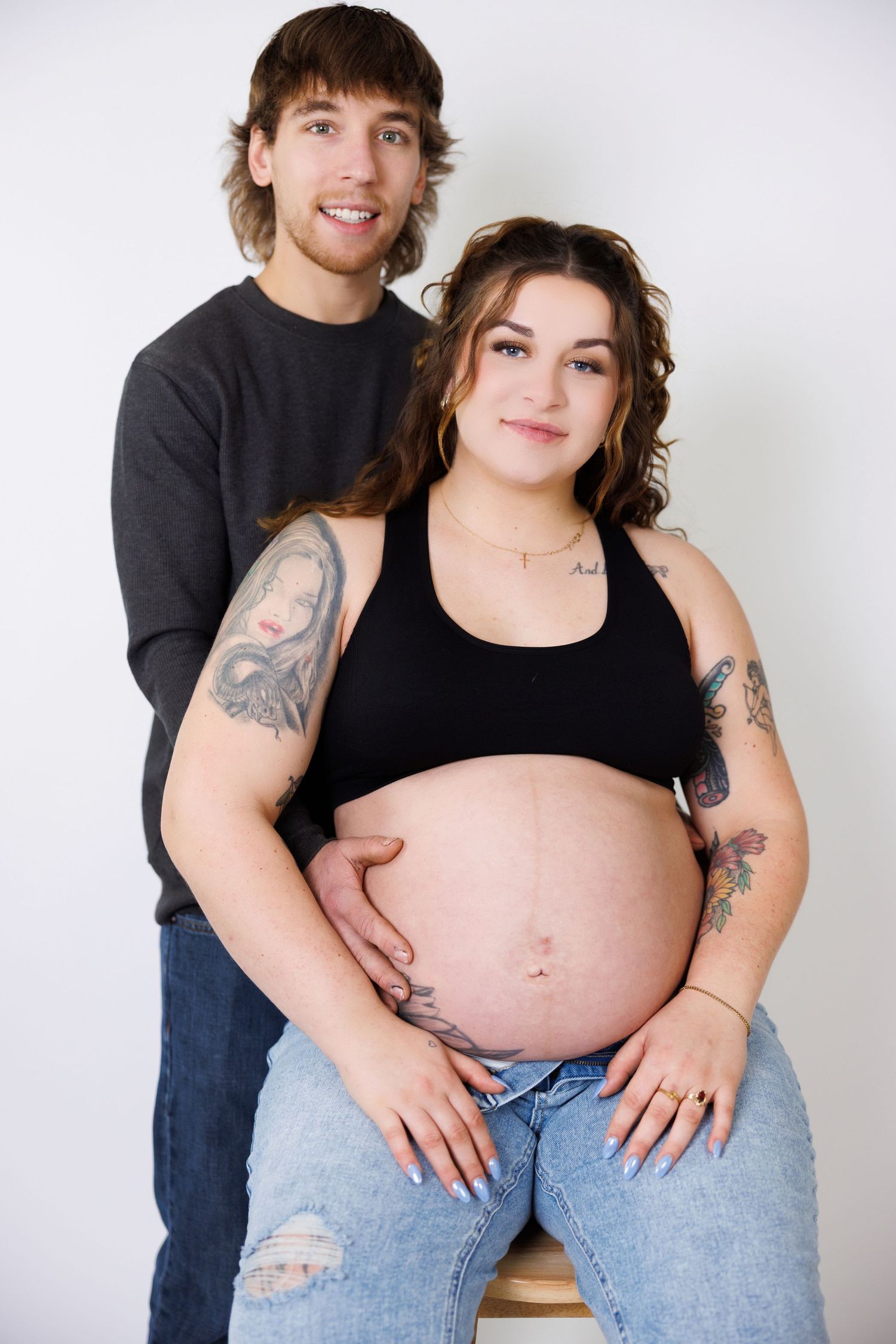An expectant couple shares an intimate moment during a maternity photoshoot in casual attire.