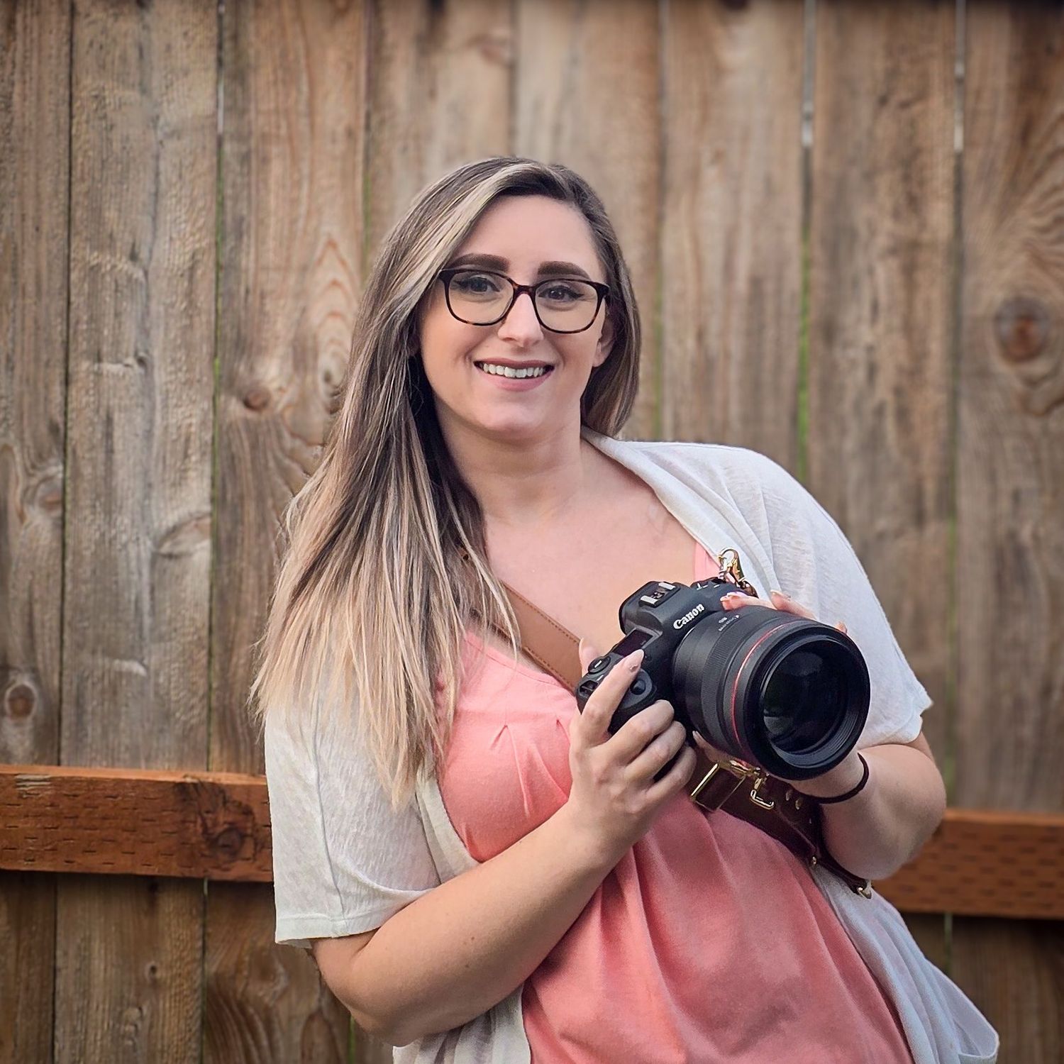 Professional photographer with camera taking outdoor portraits against wooden fence background.