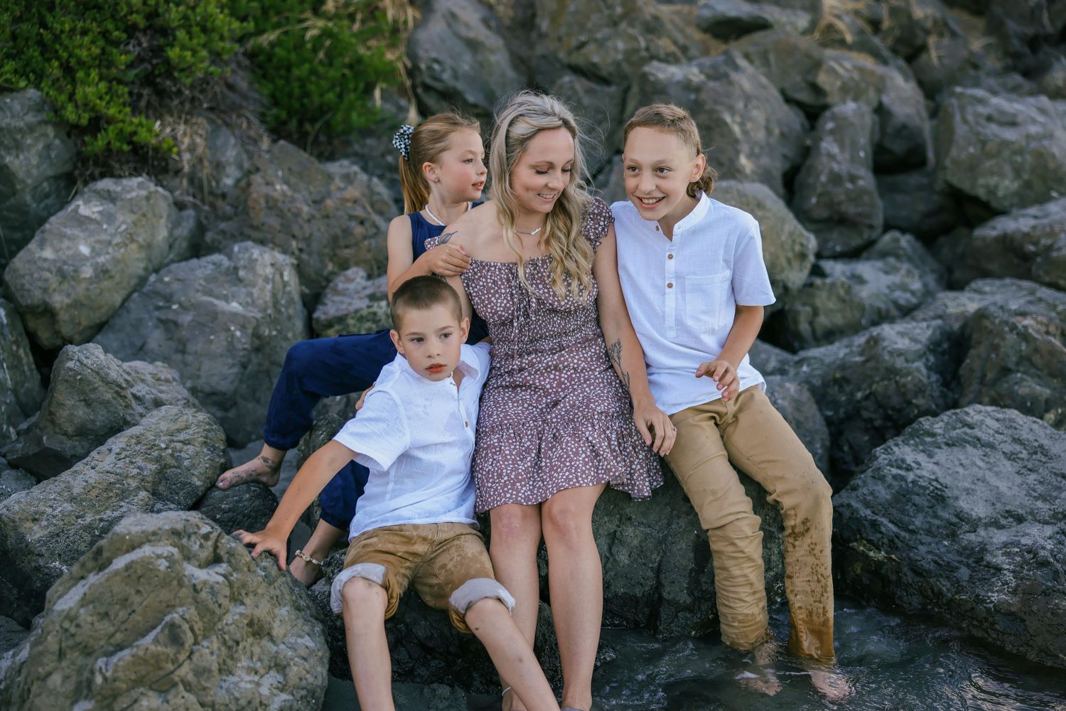 Natural candid family moments captured on rocky beach during sunset.