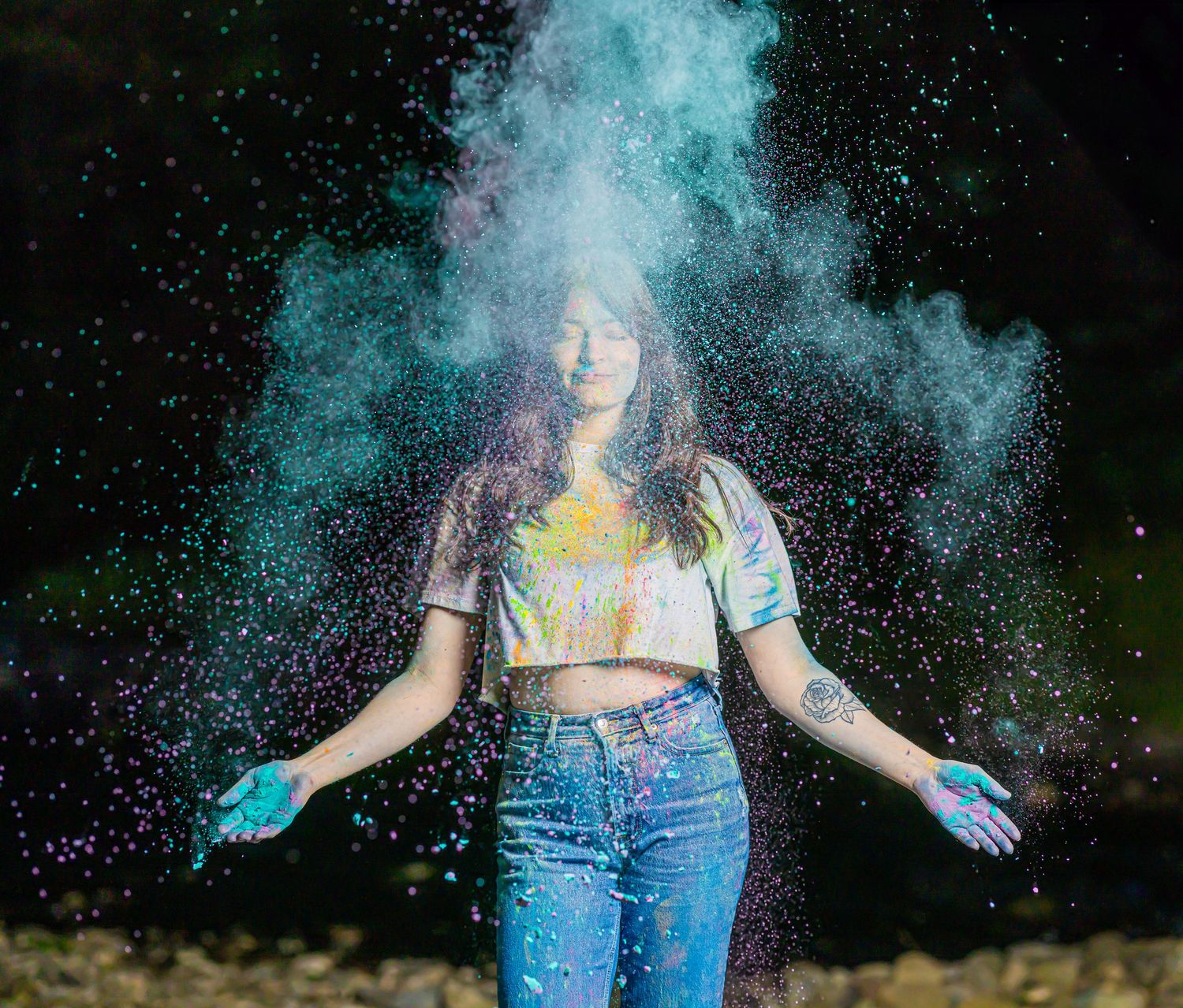 Teal powder paint explosion surrounds figure in casual denim and crop top.
