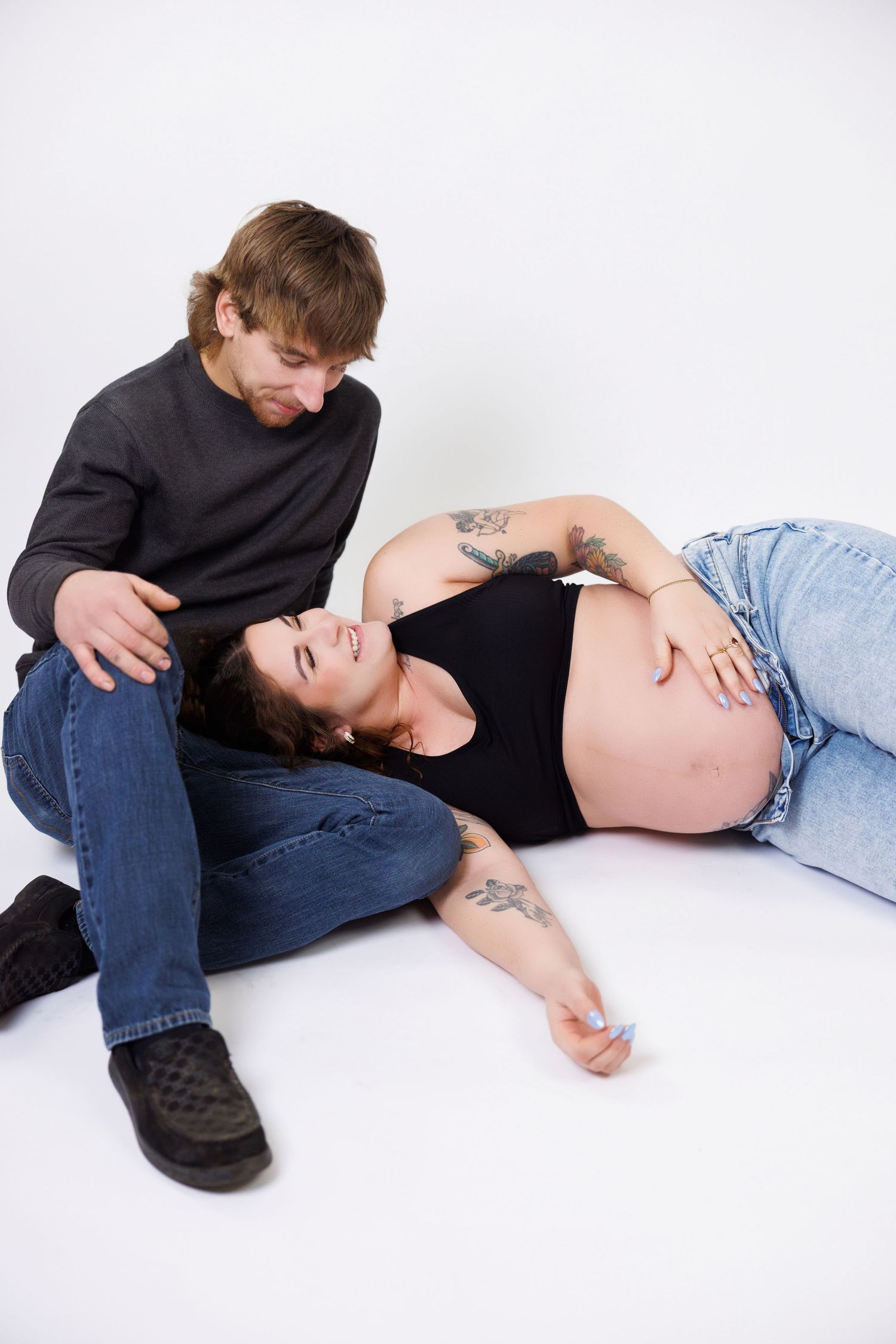 Person in dark clothing lies on white floor while holding their pregnant belly.