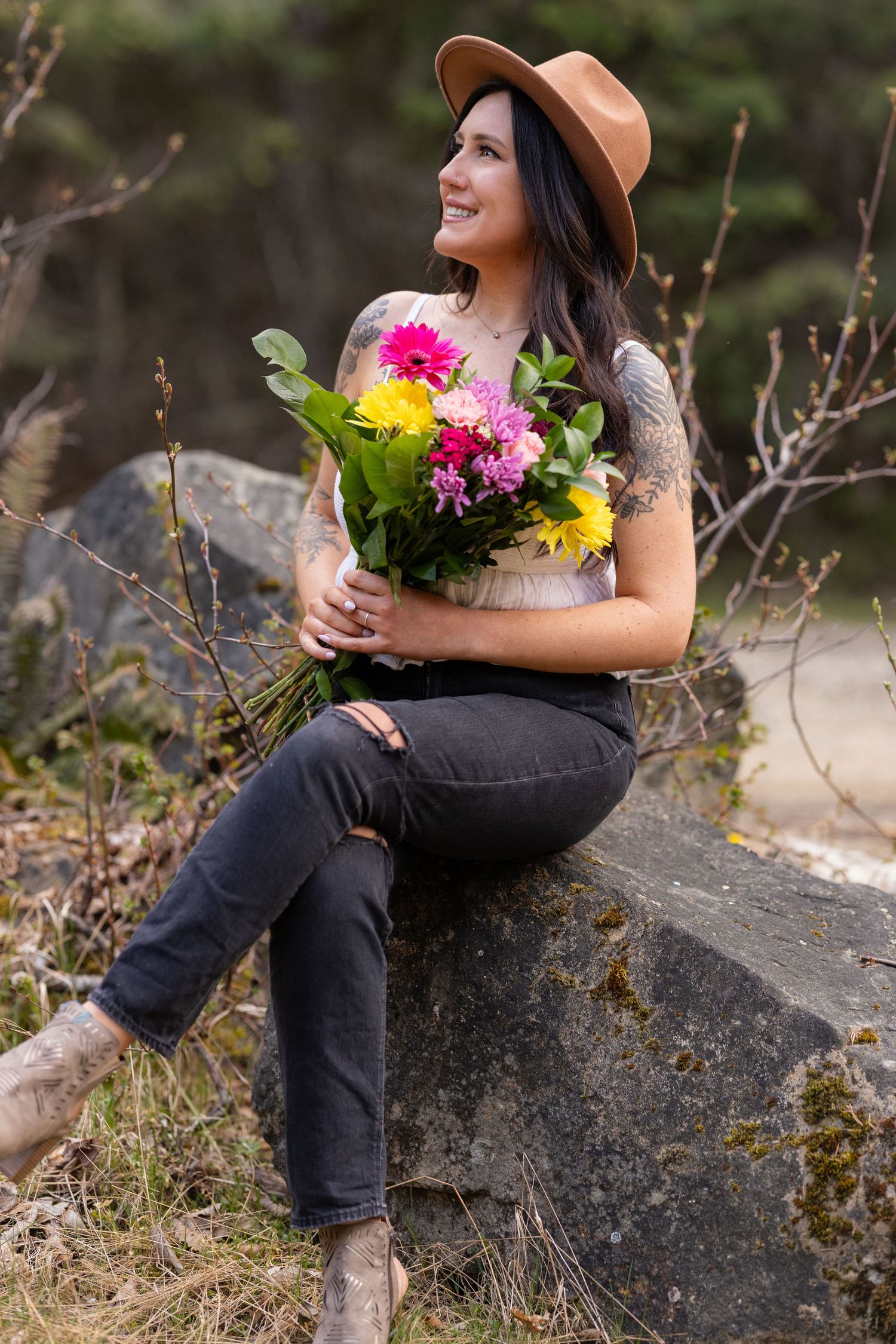 Woman sitting on rock holding bright floral arrangement in outdoor setting.