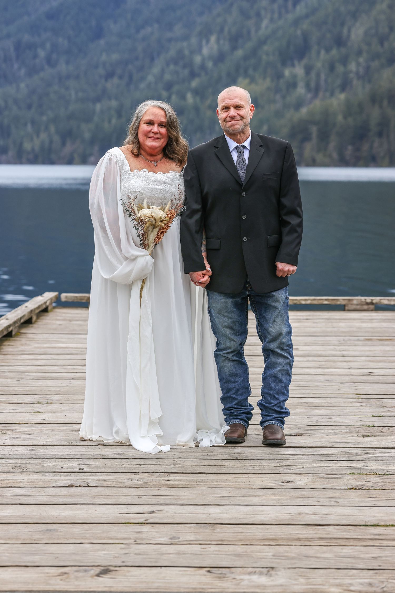 Couple stands together on wooden dock with mountain lake backdrop during intimate wedding.