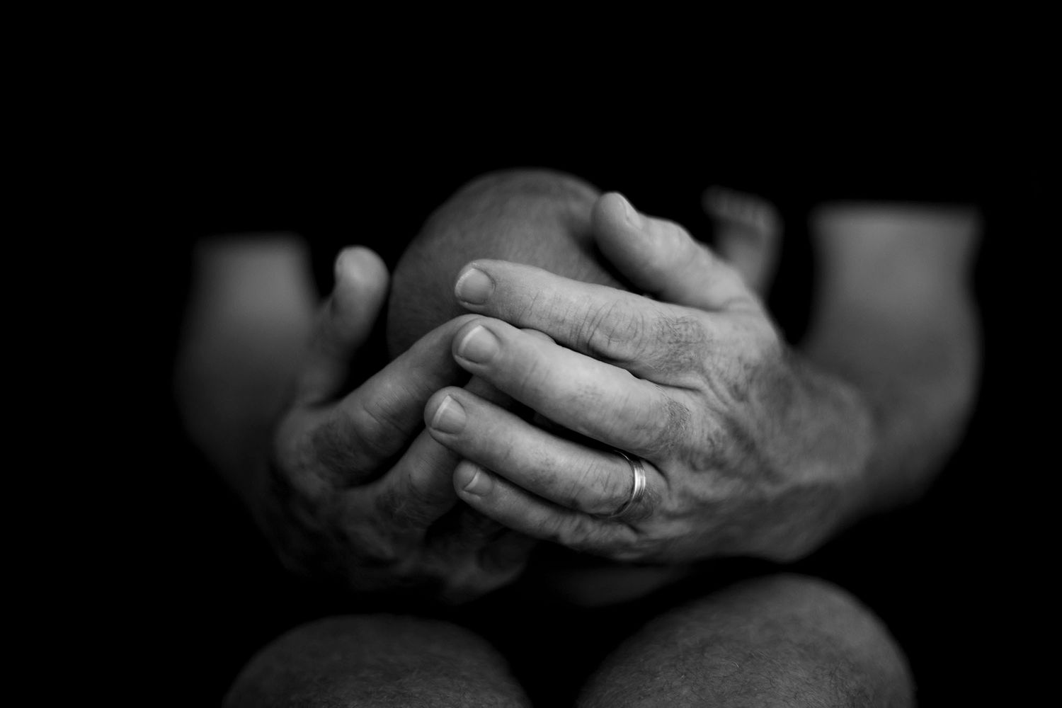 A black and white close-up of clasped hands, showing intricate details and textures in dramatic lighting.