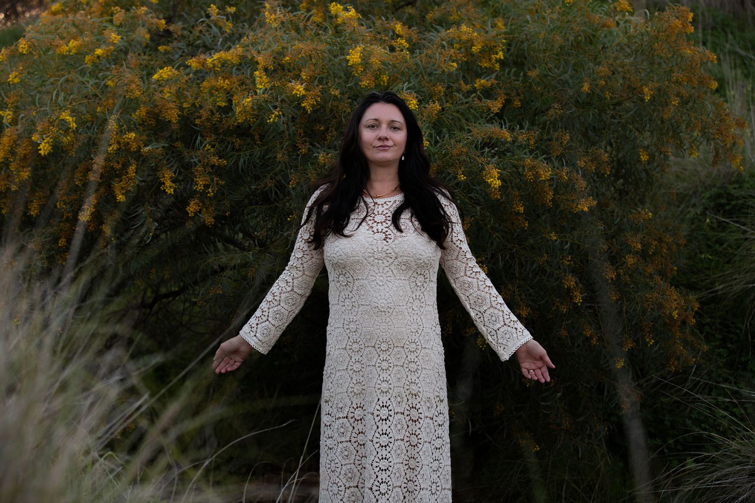 Person wearing white lace dress stands against autumn foliage at sunset.