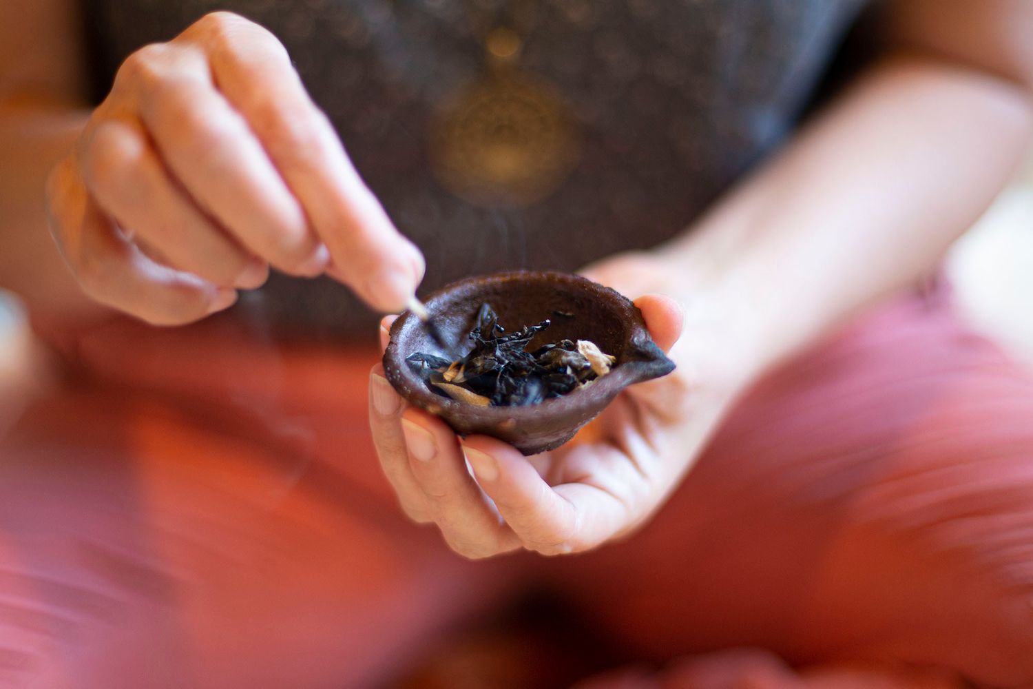 Close-up shot of hands gently grating a fresh chocolate bar using a fine grater on a red wooden surface.