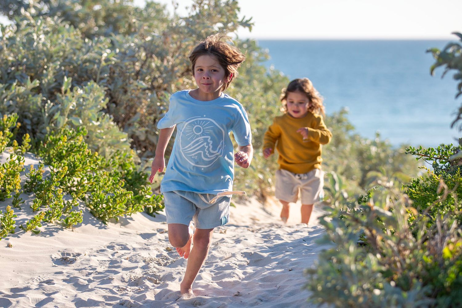 Children playing on a sunny beach with coastal vegetation and blue ocean waters.