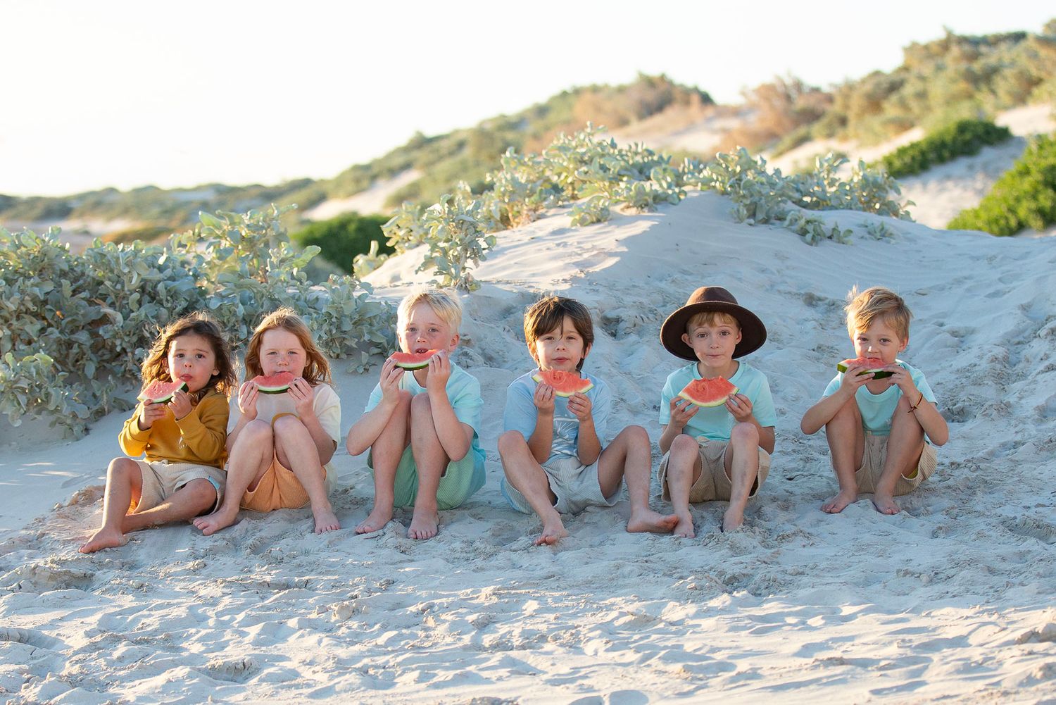 Family lying together on beach sand at sunset.