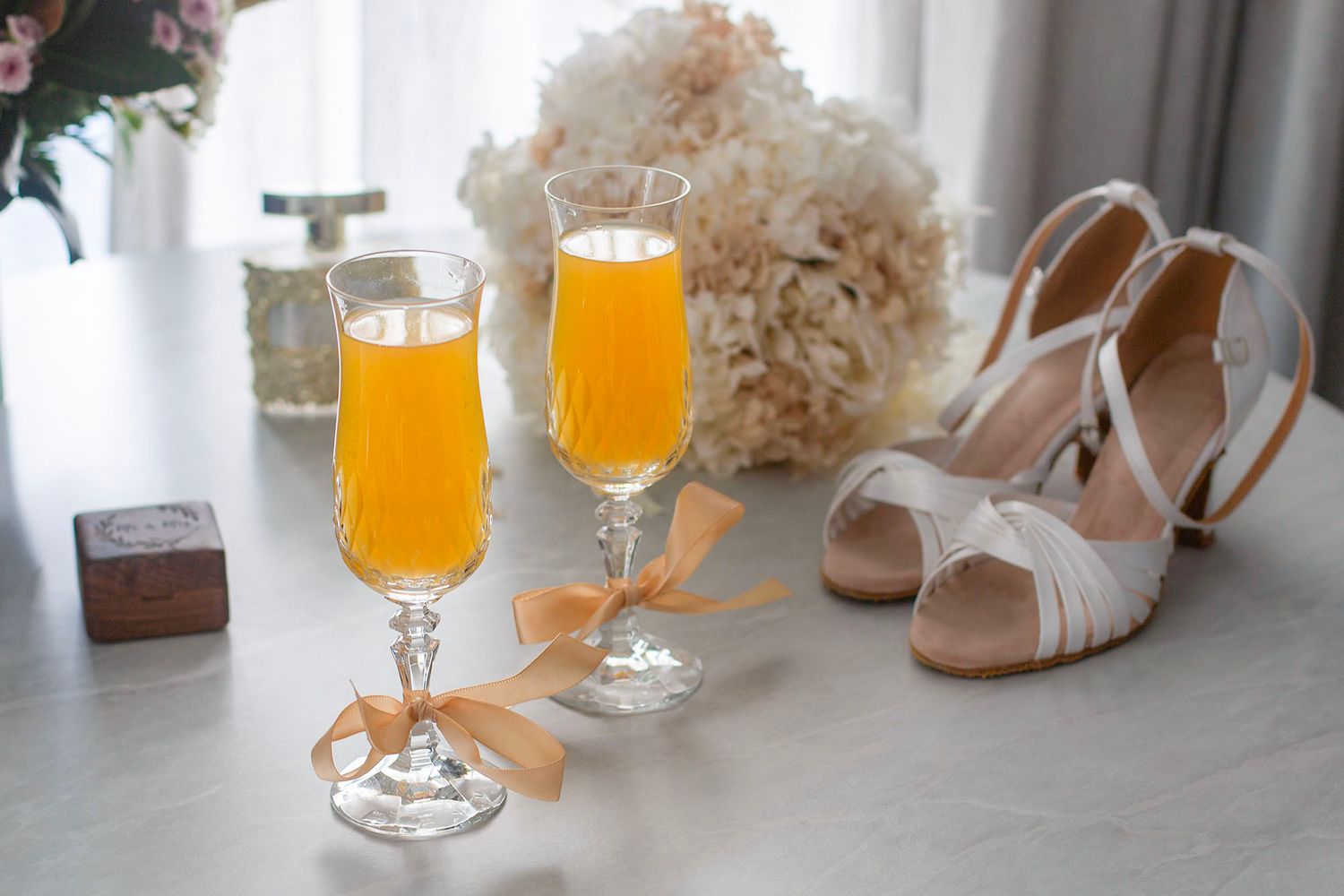 Wedding reception setup with orange juice glasses and white hydrangeas on a light table.