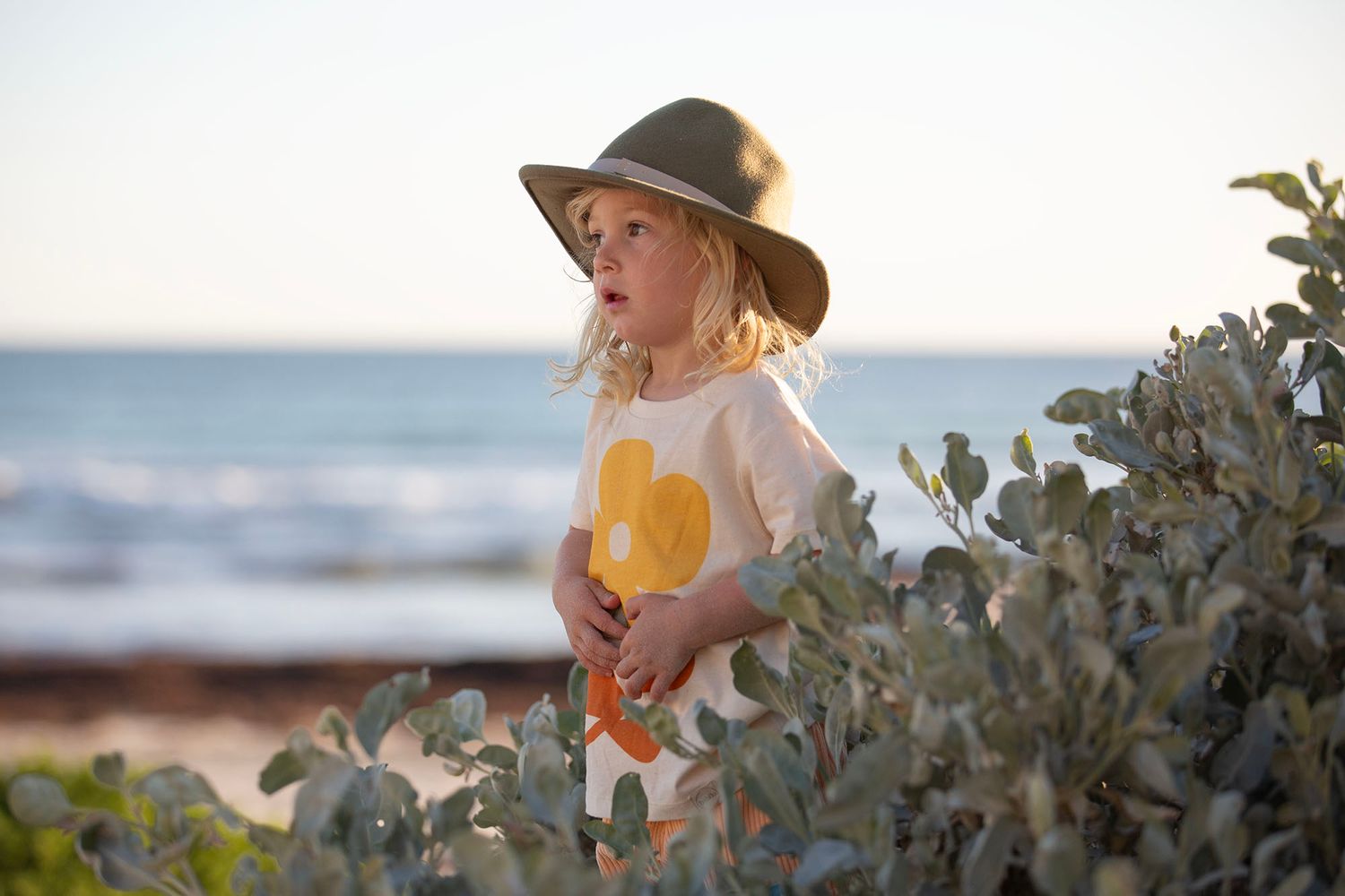 Children exploring coastal vegetation on sandy beach during sunset.