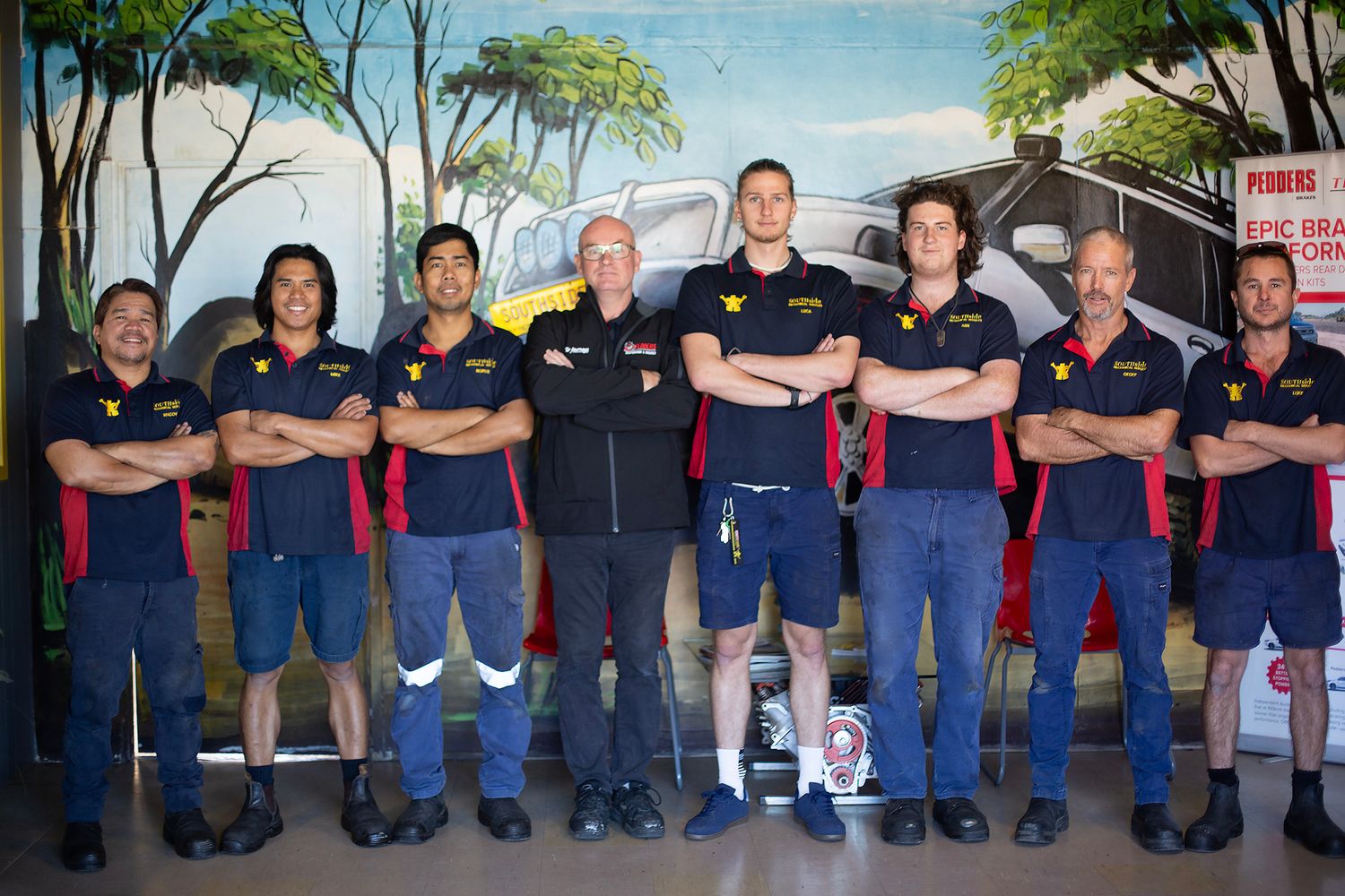 Group photo of work colleagues standing against an exterior wall wearing uniforms.