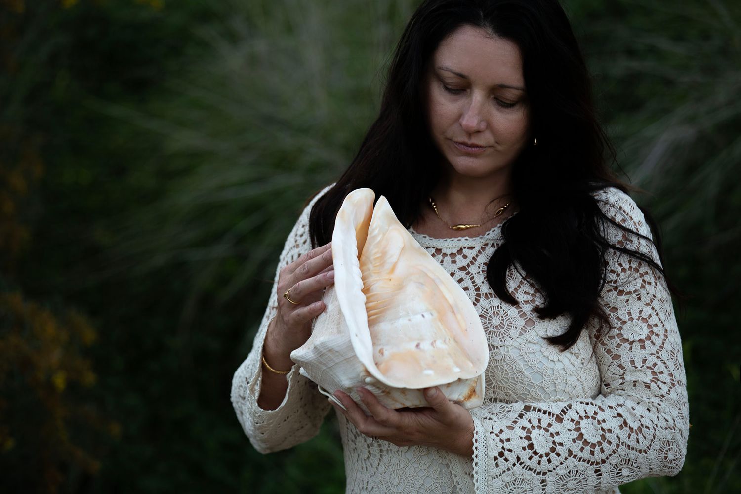 Woman in white lace dress poses in an outdoor nature setting.