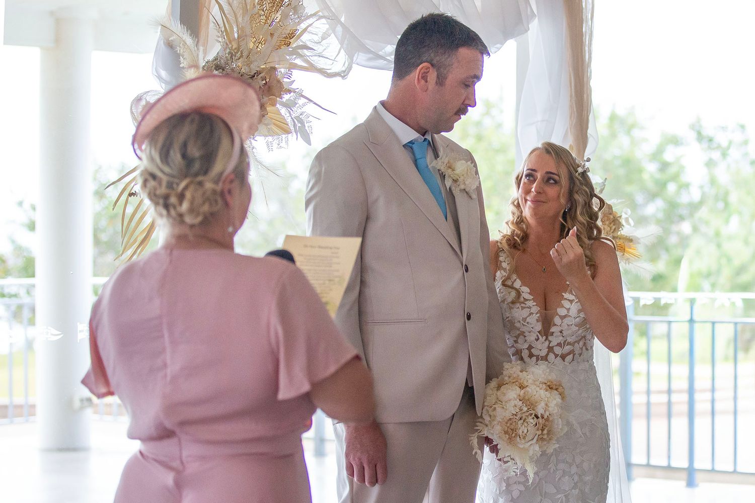 Wedding ceremony participants line up in a bright indoor venue with flowing curtains.