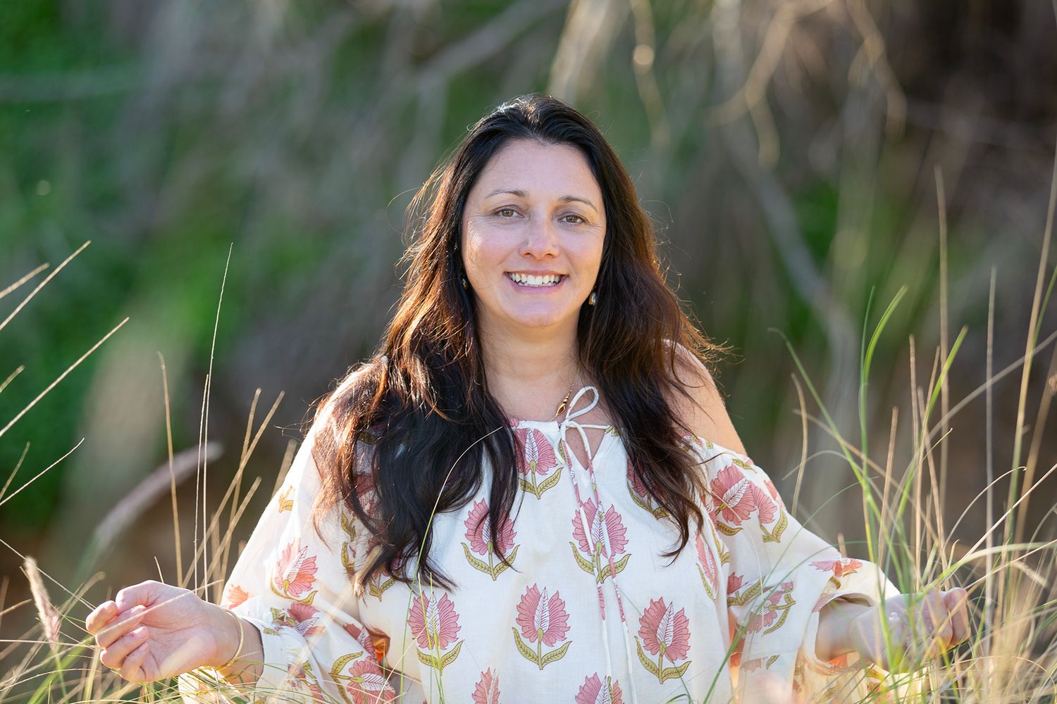 Someone sitting in tall grass wearing a white embroidered dress during golden hour.