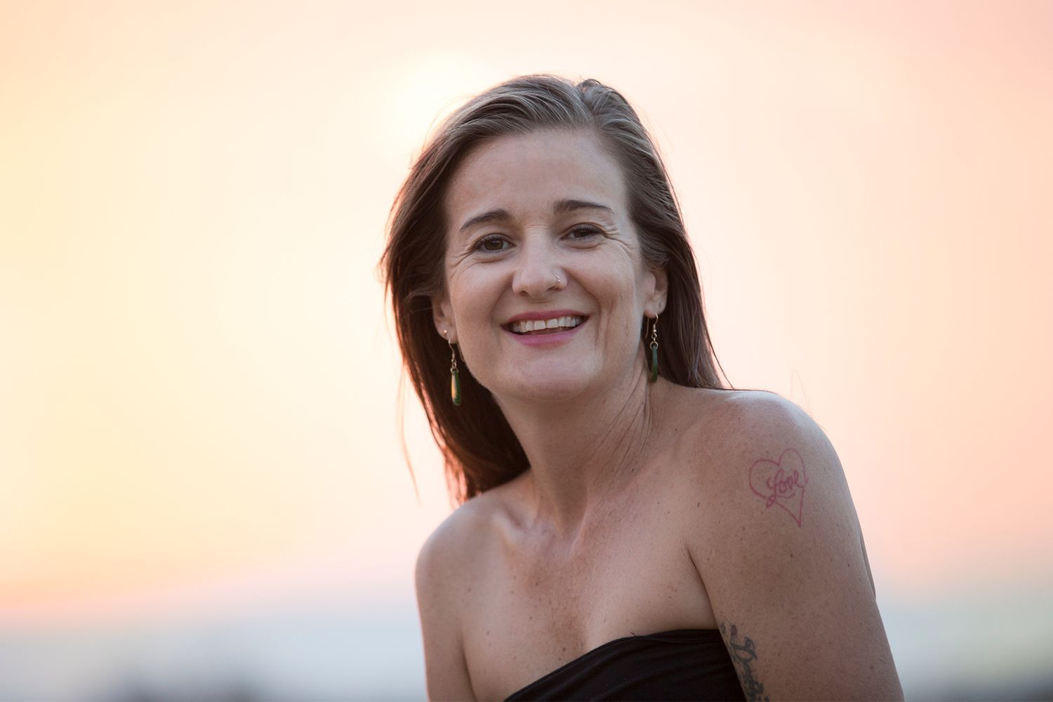 Someone laughs joyfully while posing outdoors at sunset with a warm glowing background.