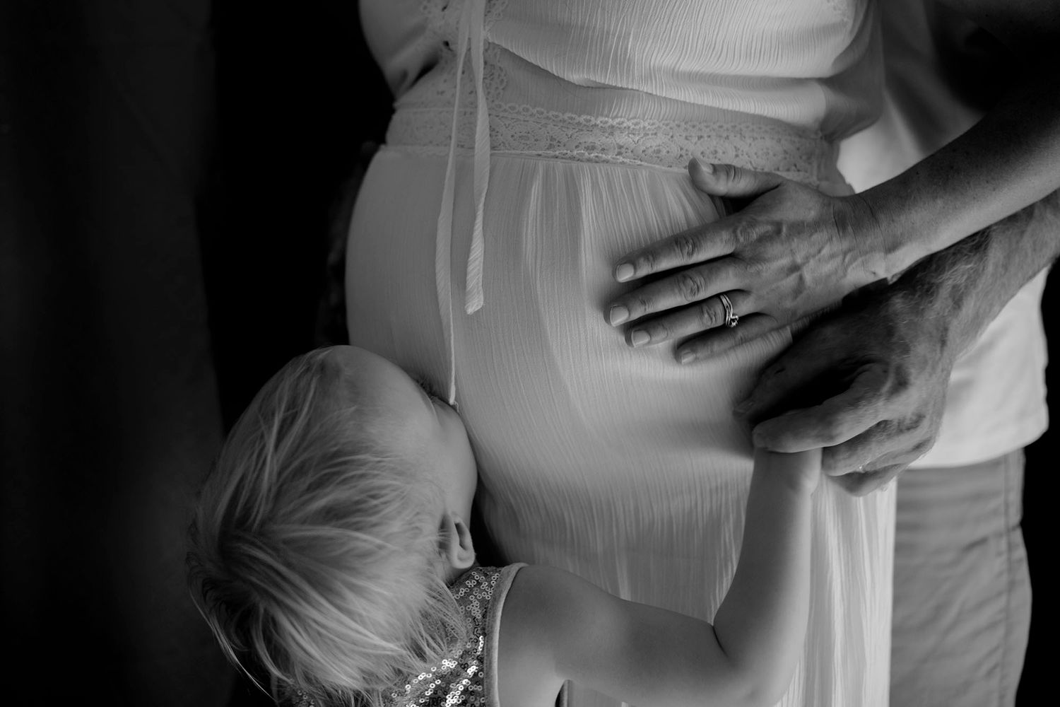 Black and white artistic maternity photo with gentle hands on belly.