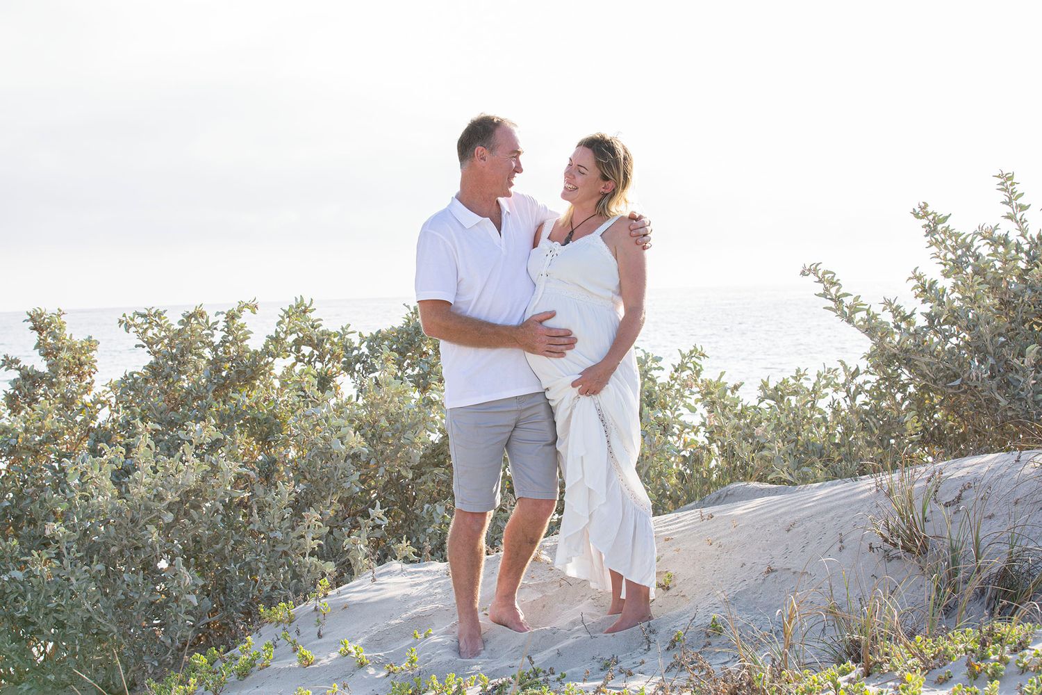 Family in white outfits shares intimate moments on coastal rocks.