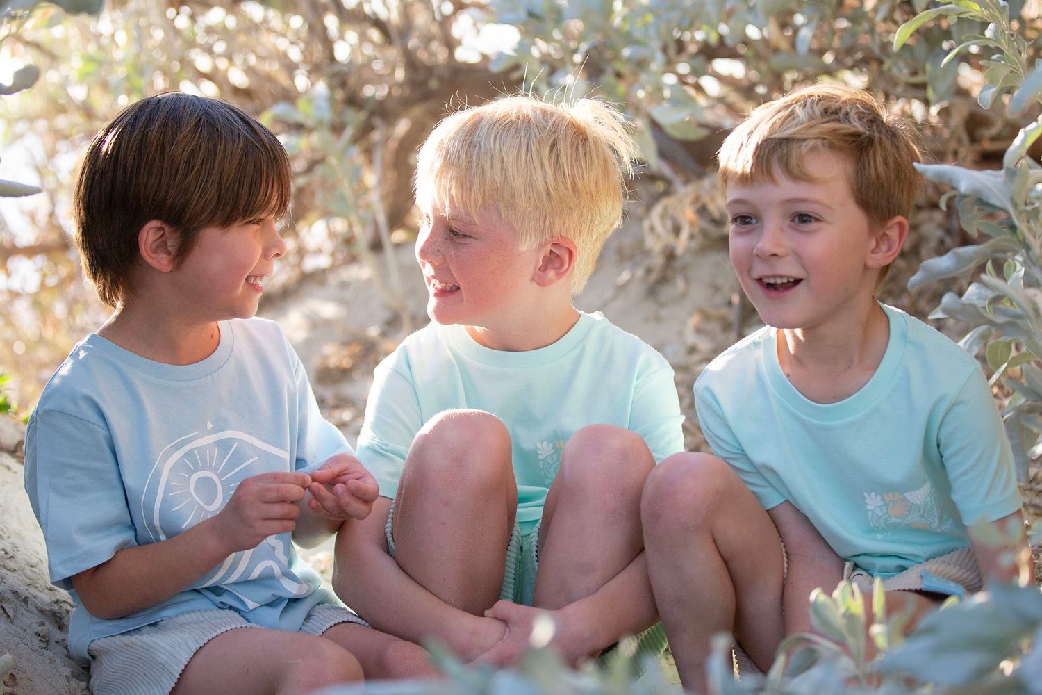 Children sitting together on beach sand during golden hour.