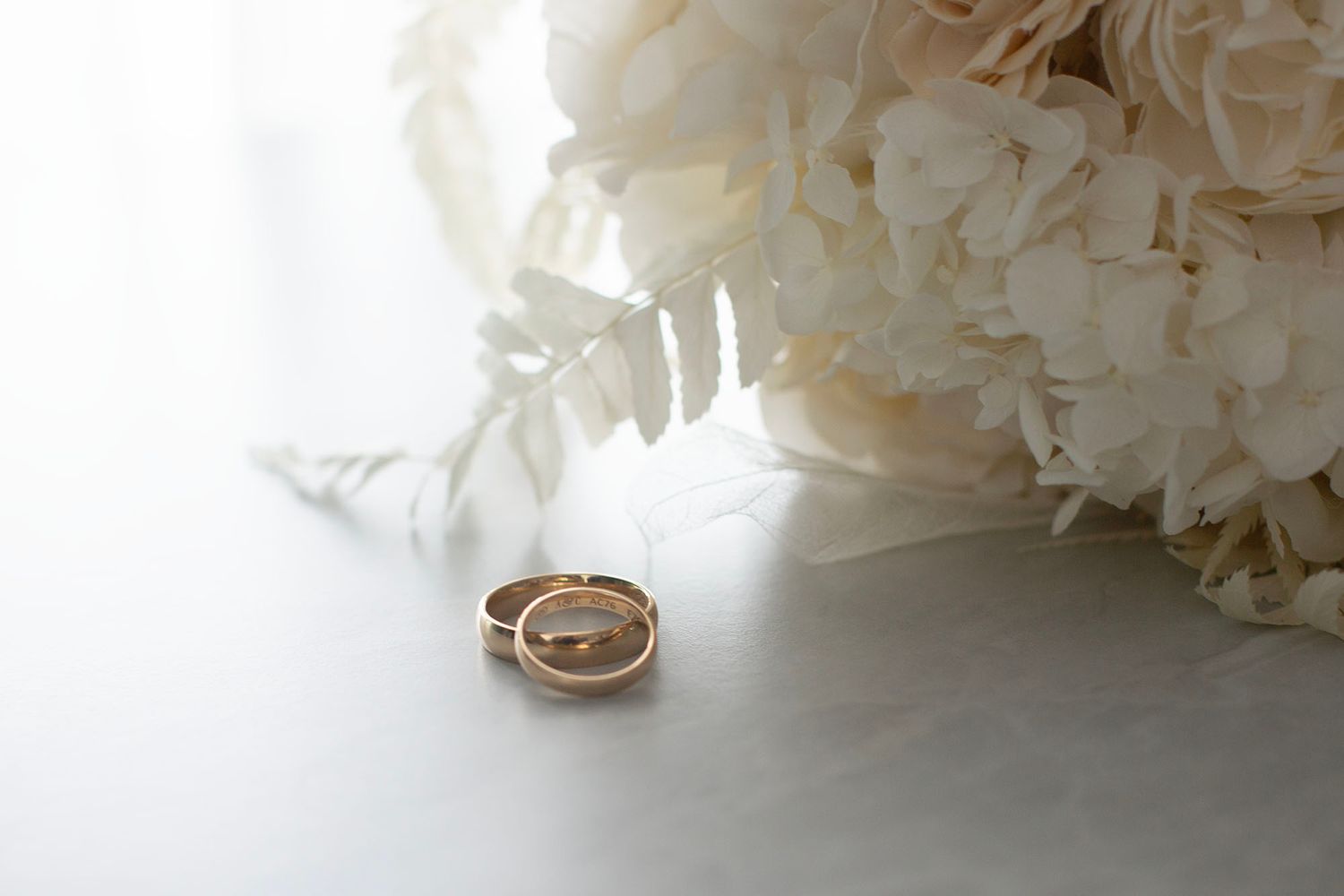 Wedding rings displayed with soft white floral arrangements in background.