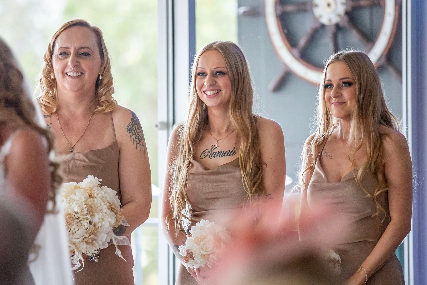 Bridesmaids in matching dresses react with joy during a wedding ceremony.