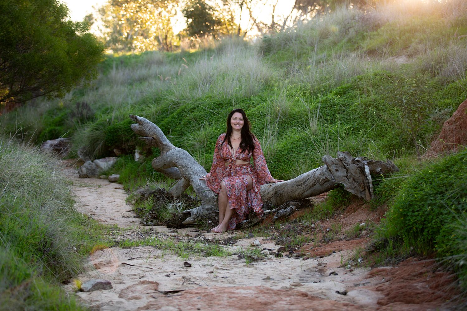 Woman in a floral dress poses outdoors against a natural backdrop during golden hour.