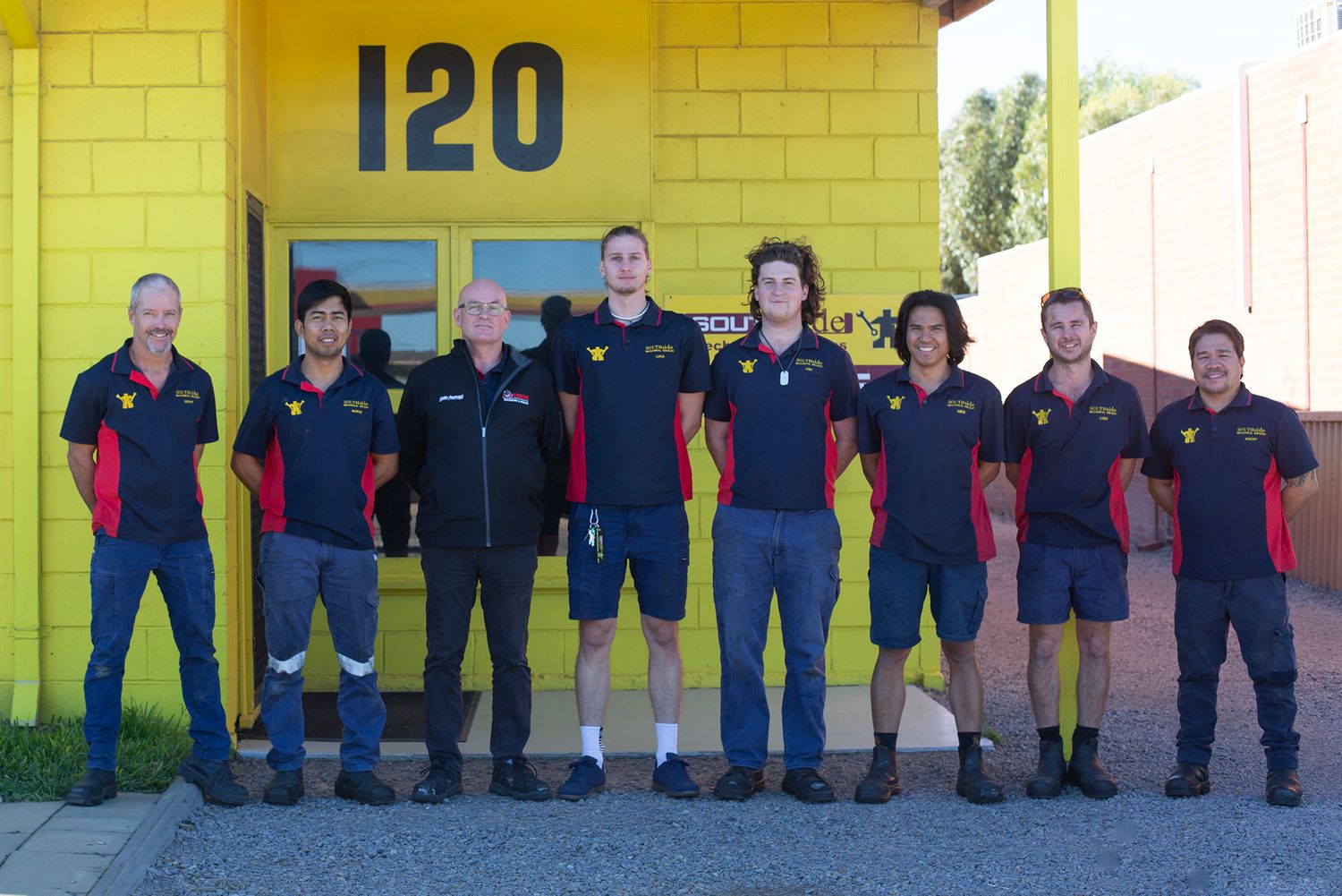 Row of uniformed workers lined up against a yellow wall with room numbers.