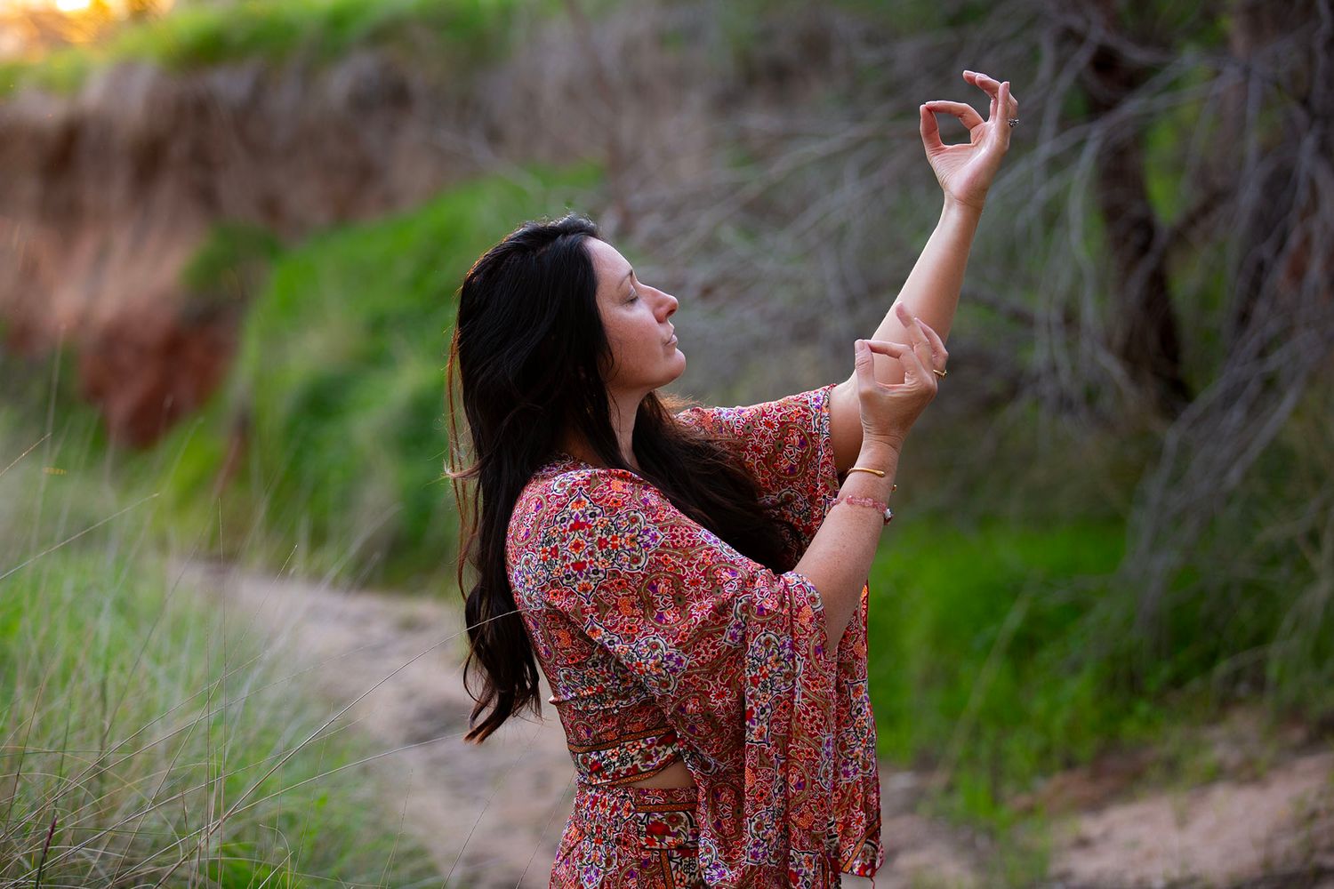 Woman in a flowing floral dress dances gracefully in a natural outdoor setting.