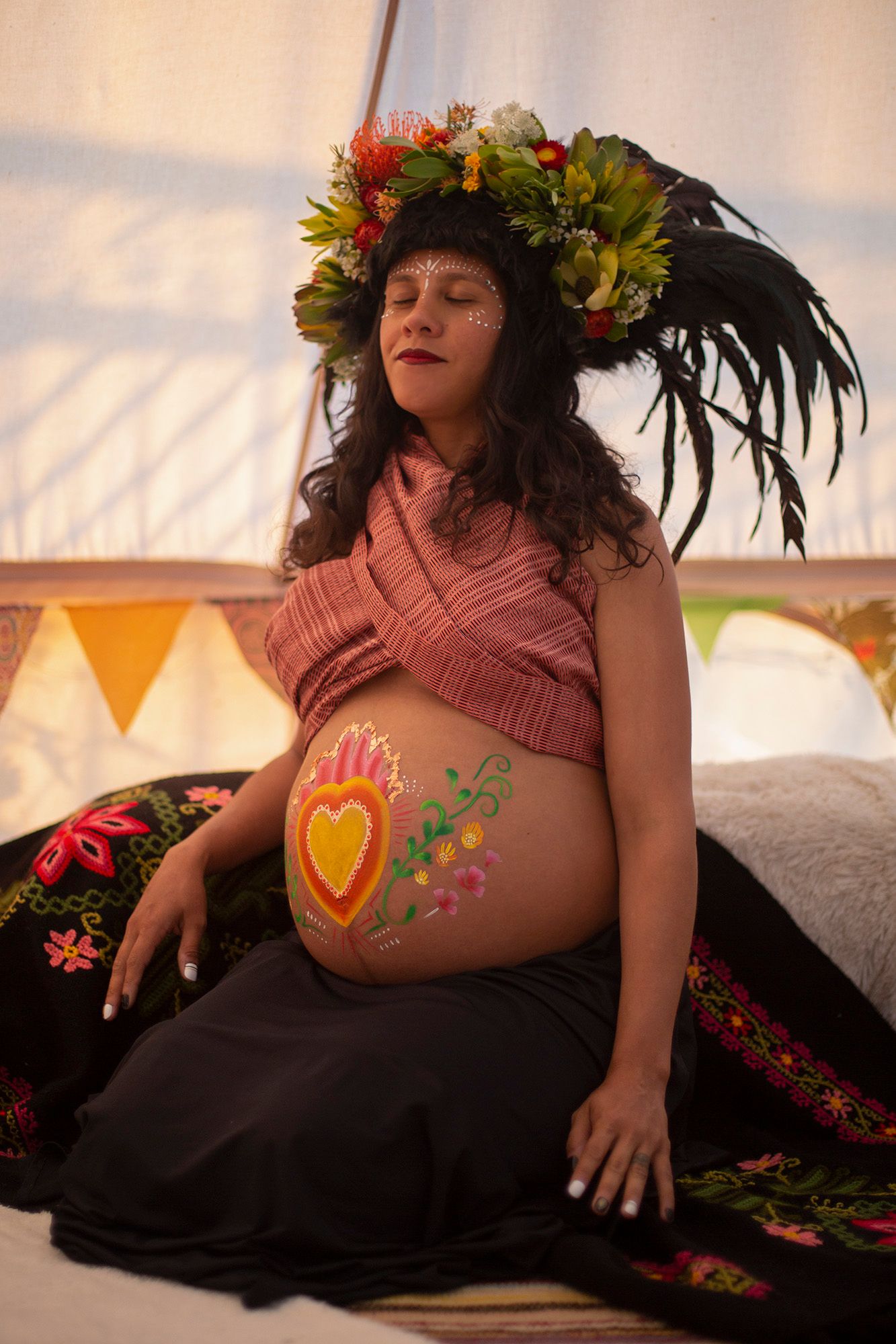 Artistic maternity portrait with floral crown and belly art in boho setting.