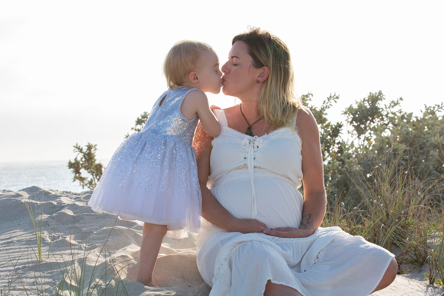Series of tender mother and child portraits in white dresses on beach.
