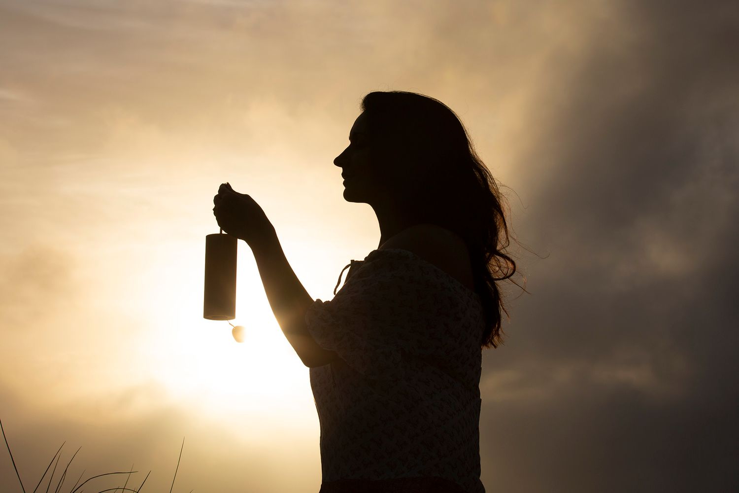 A silhouette stands against a dramatic yellow sky with trees in the background during sunset.