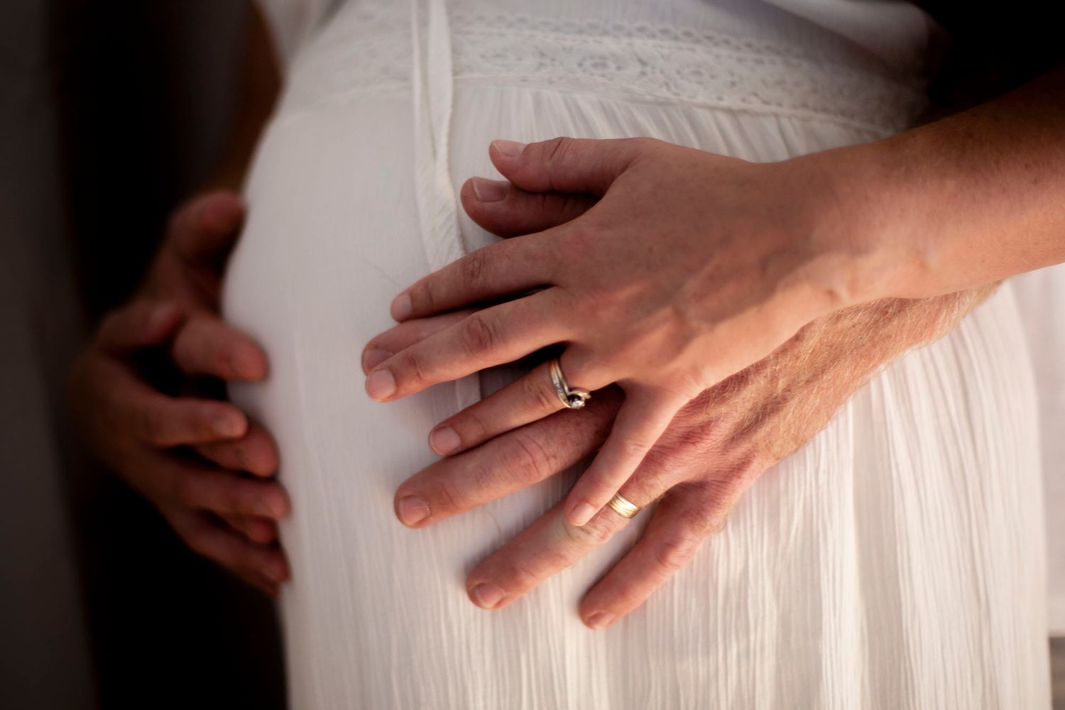 Close-up of hands resting on white maternity dress showing wedding ring.